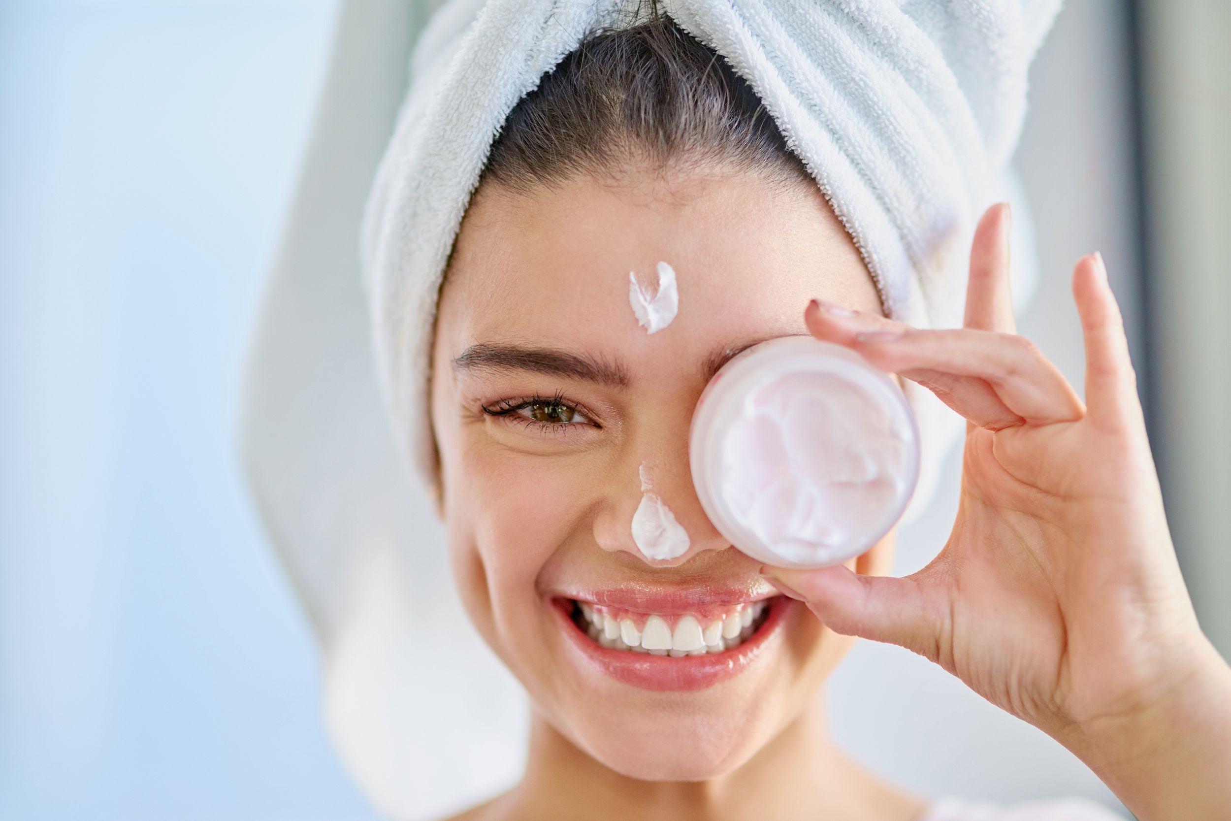 happy woman smiling with skin cream tube covering one eye