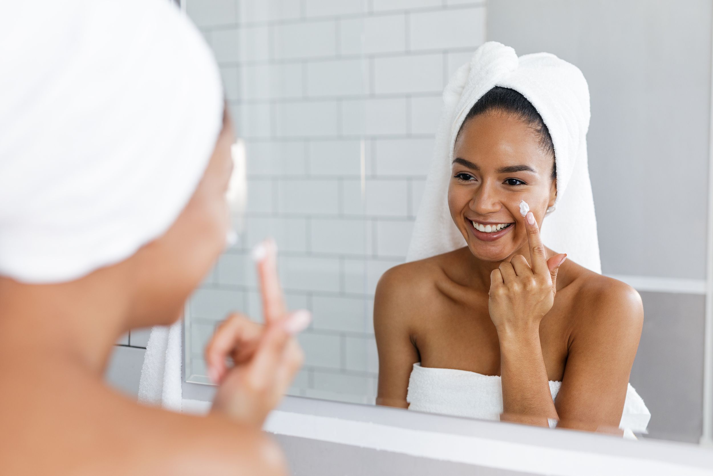 smiling woman applying moisturizer to her face in the bathroom