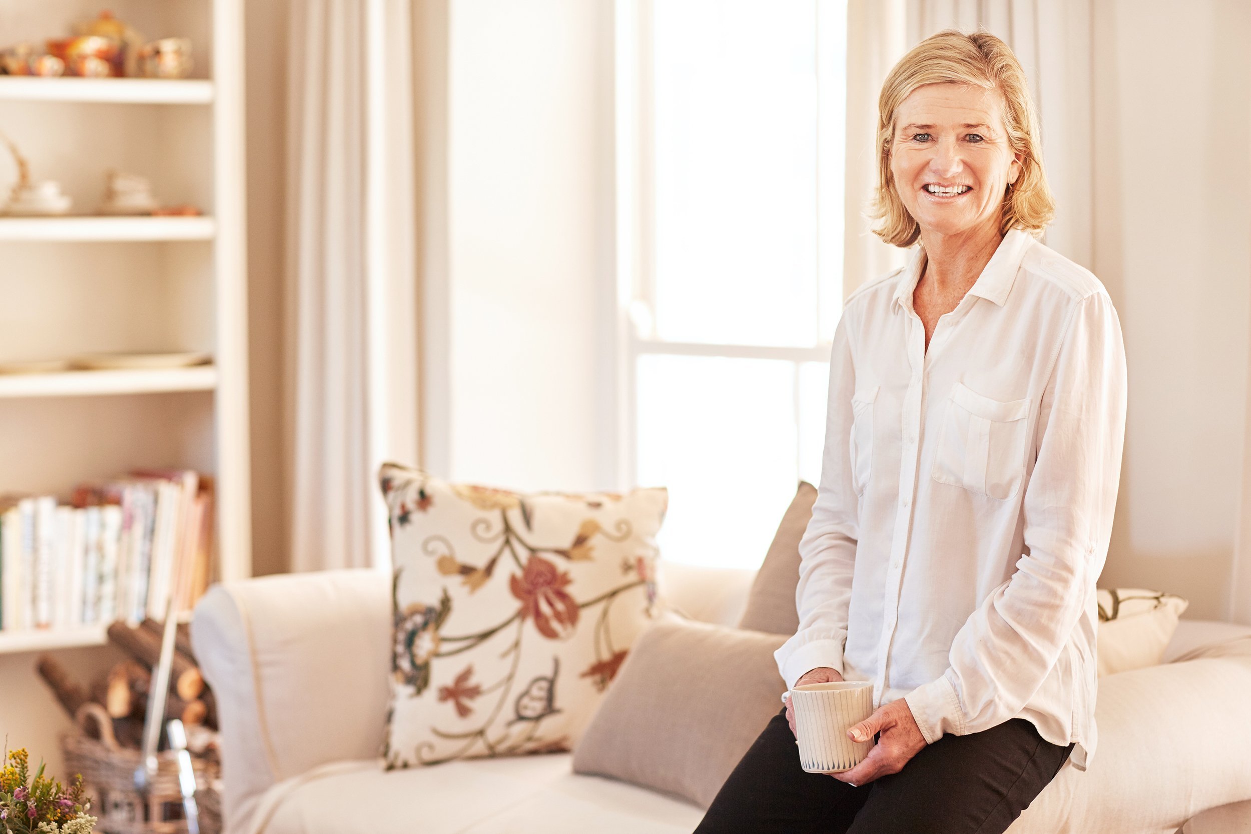 senior woman smiling and sitting casually on the arm of her couch