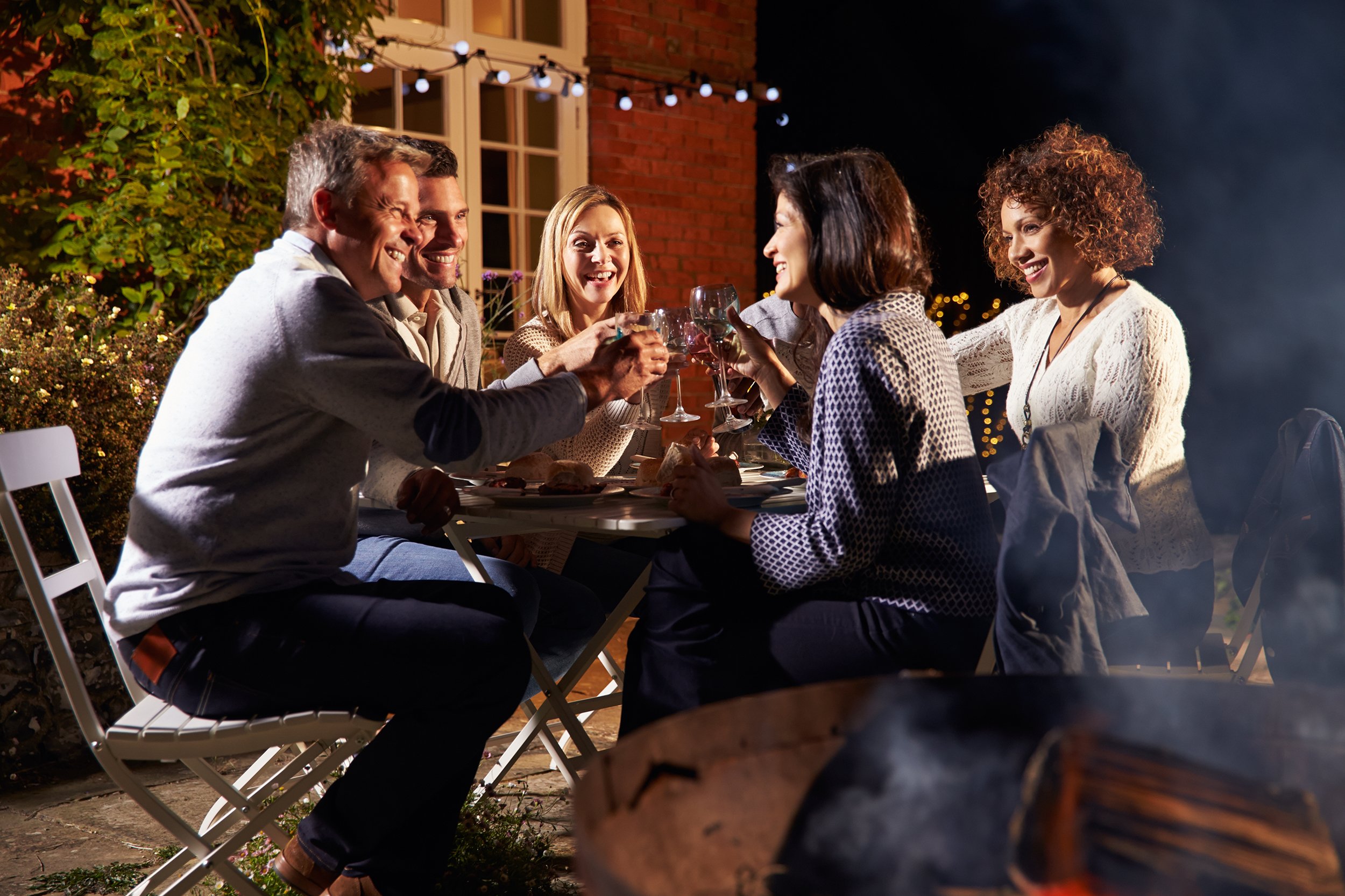 mature friends enjoying outdoor evening meal around fire pit