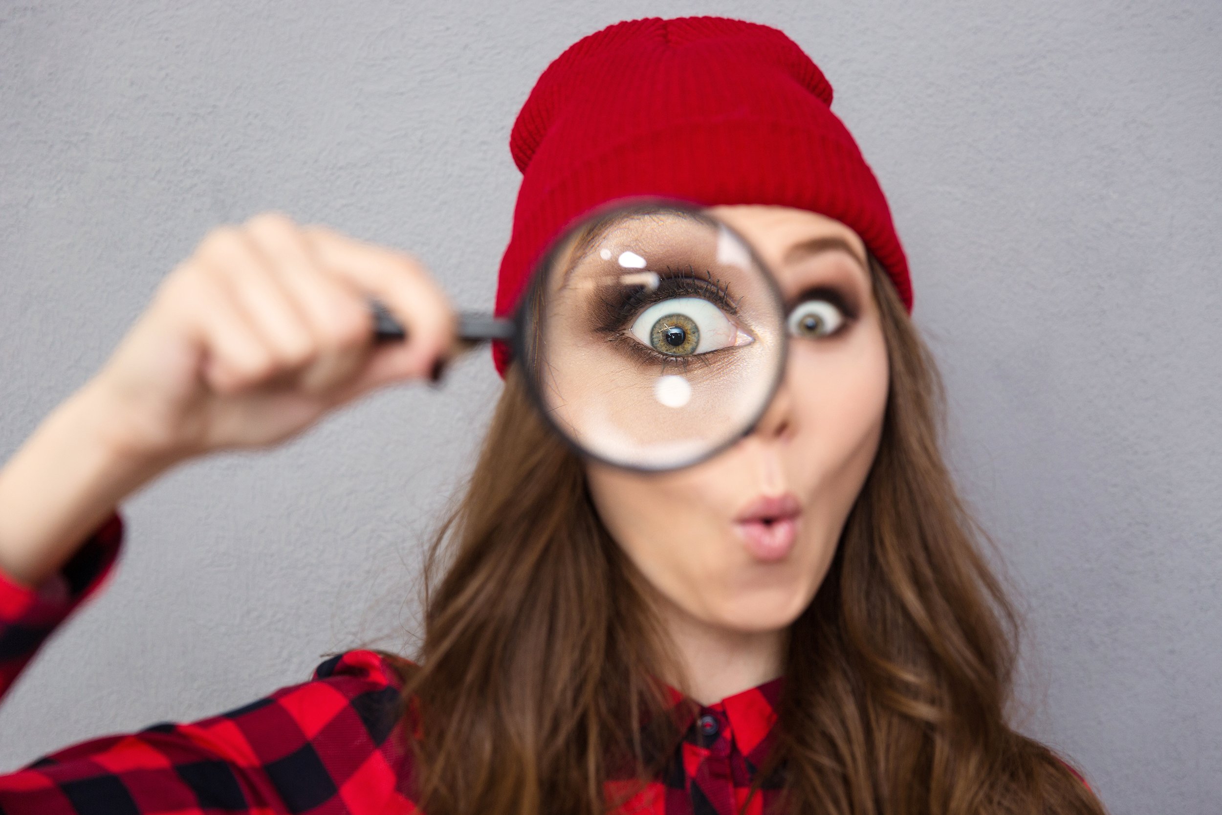 funny young woman looking at the camera through magnifying glass