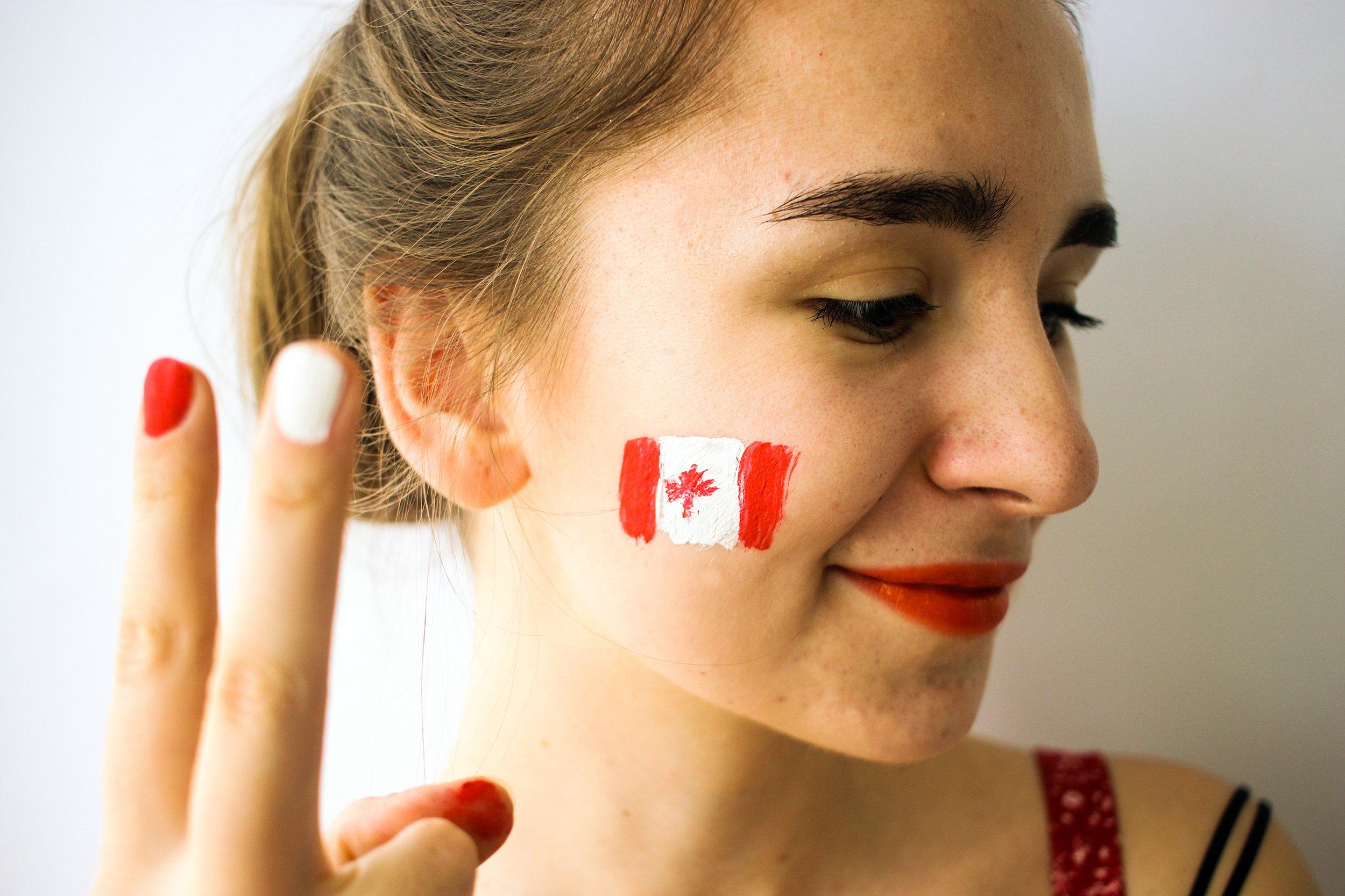 young woman with Canadian flag on cheek and red & white manicure sport fan