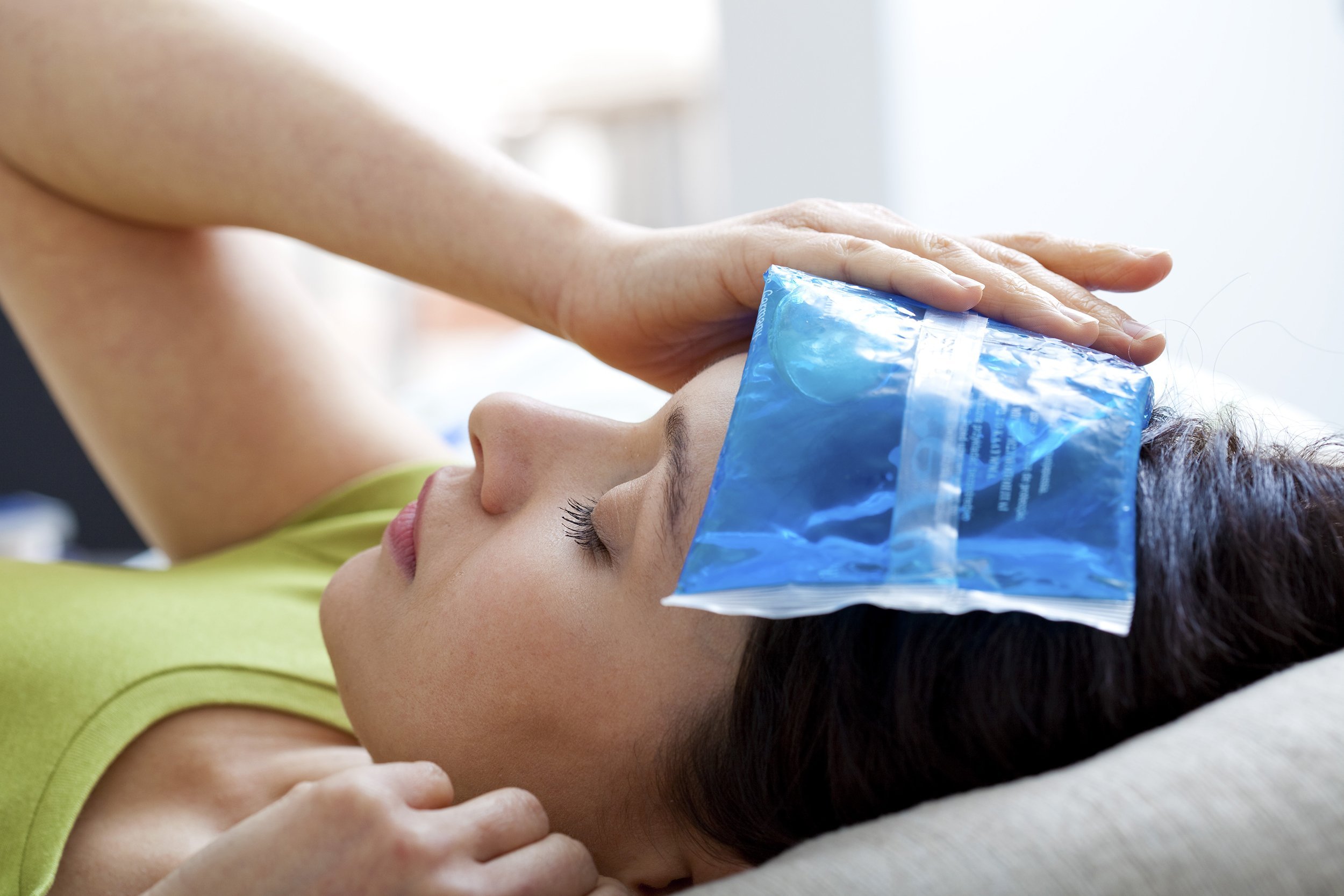 woman with cool compress on her head while lying down
