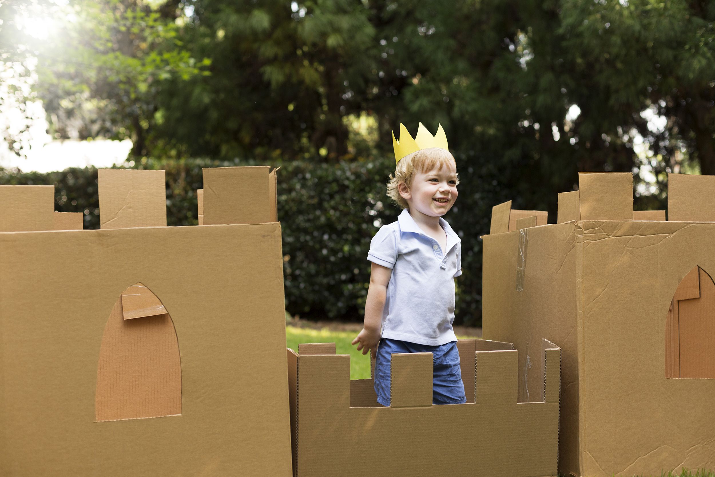 Little boy in a cardboard fort outside