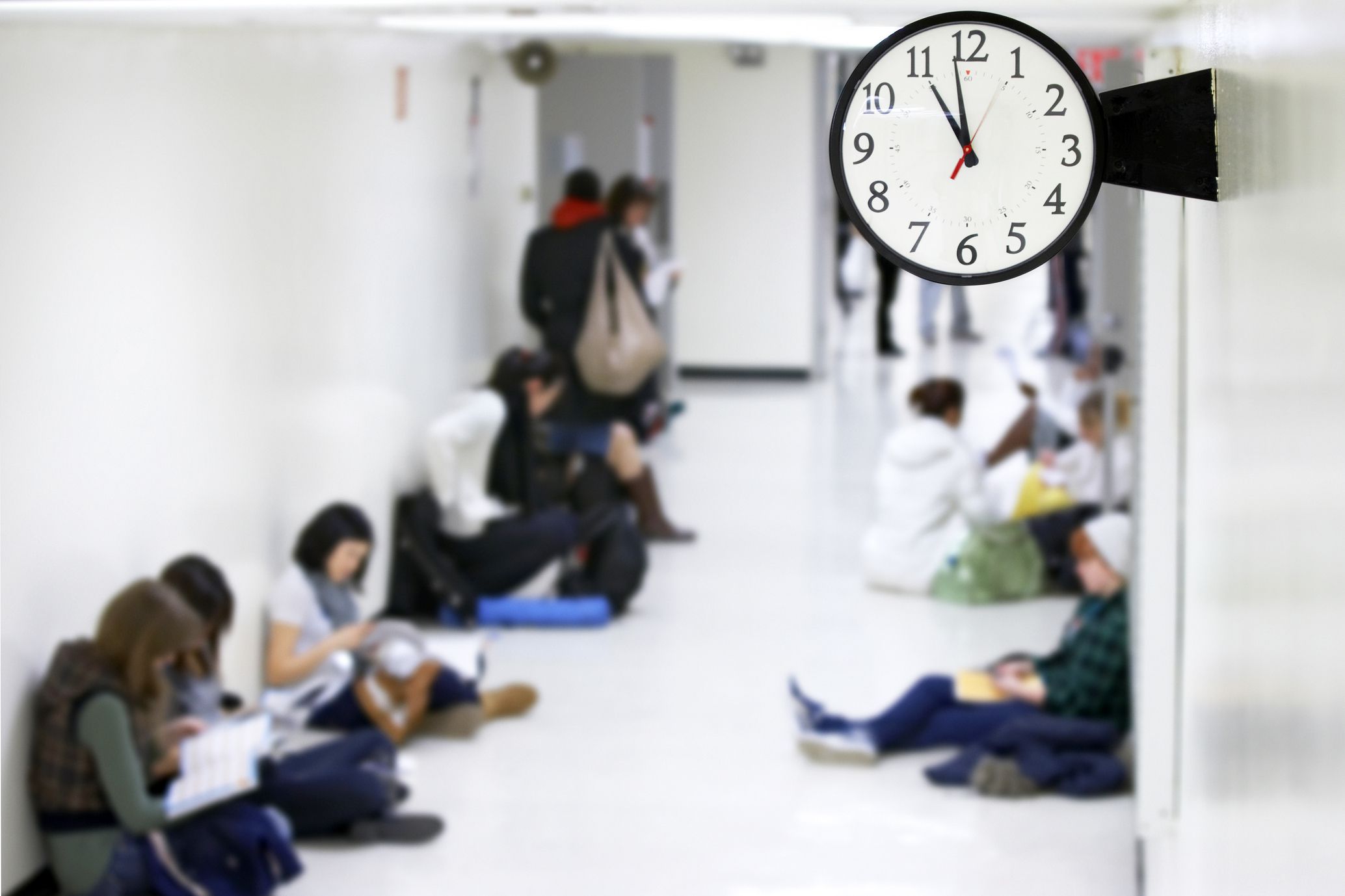 Closeup of clock in a school with kids sitting in the hallway