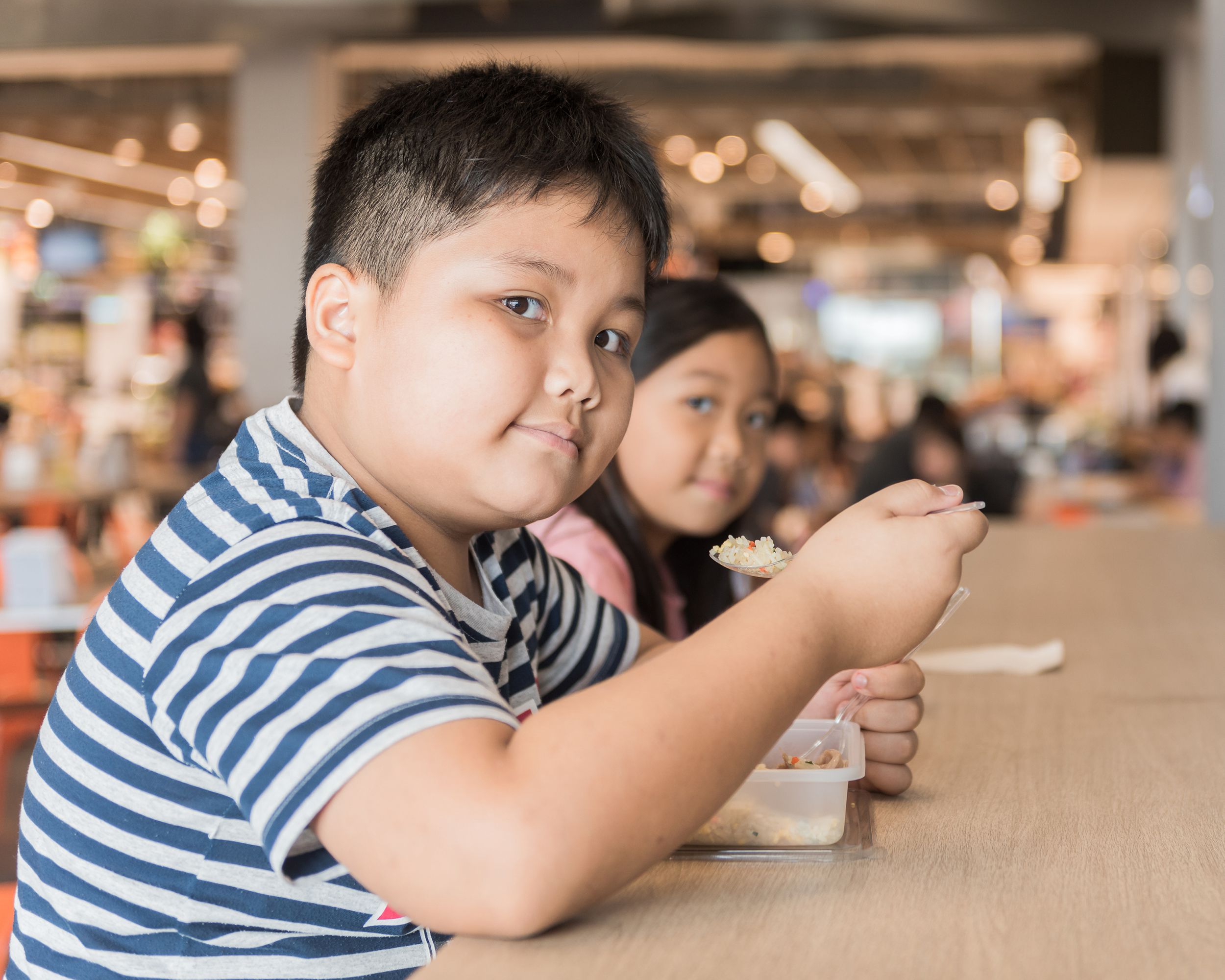 obese brother and sister eating box lunch in food court
