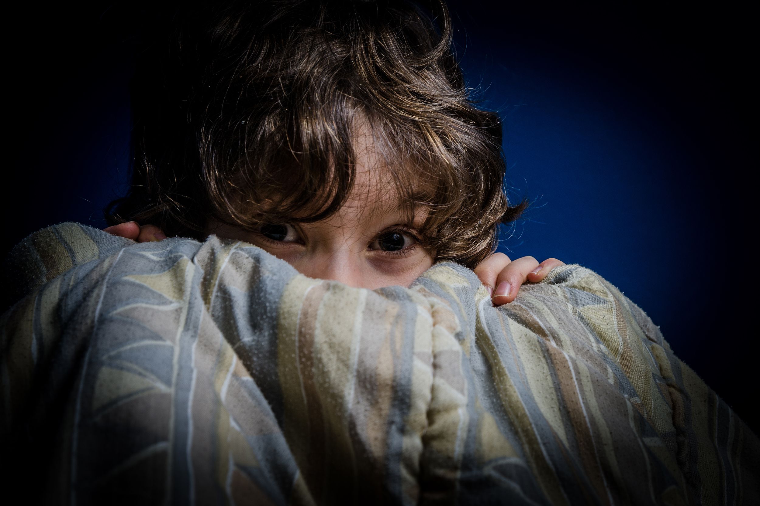 little boy afraid hiding behind his bed sheets