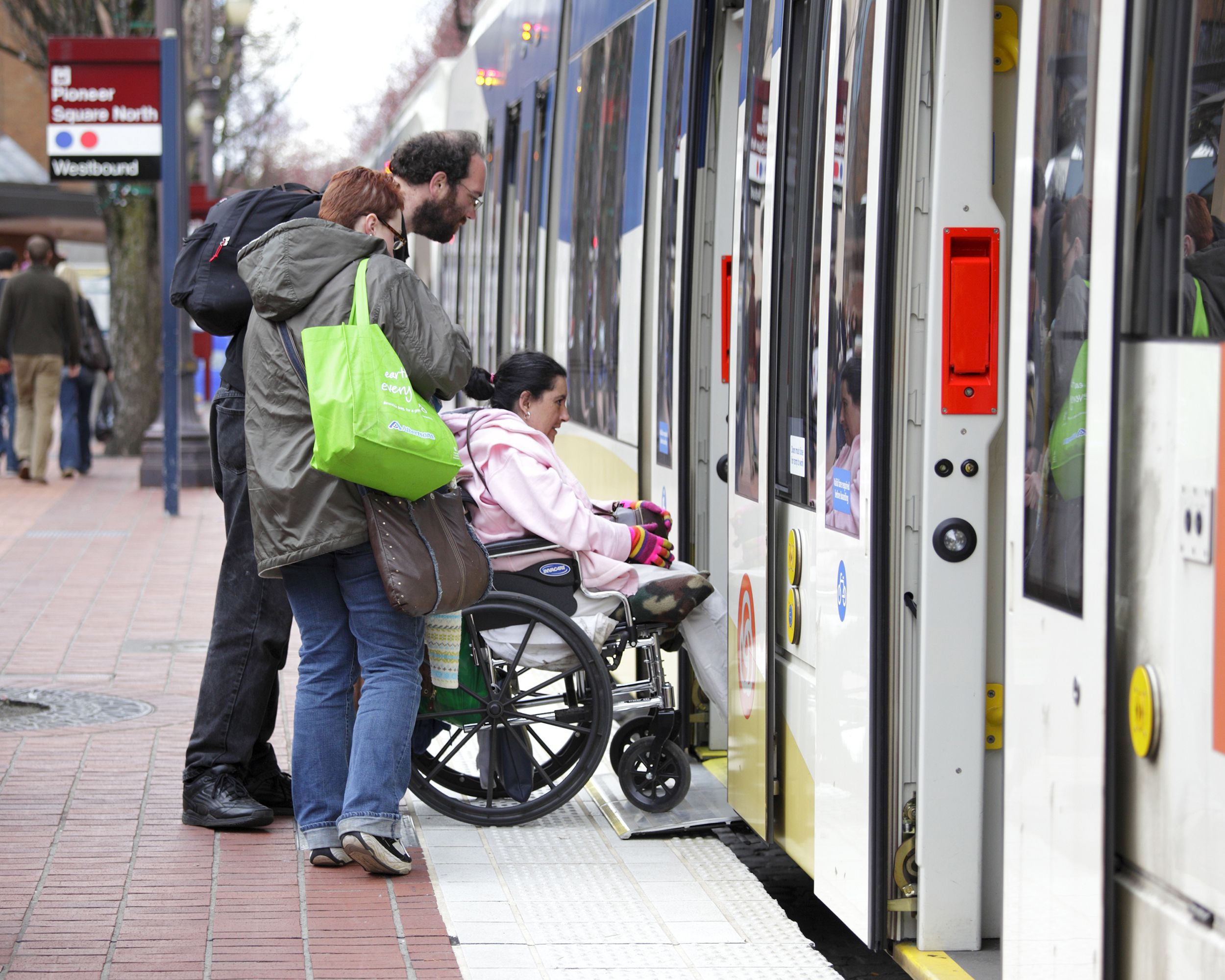 two adults push another in a wheelchair onto the train with wheelchair access in portland, oregon
