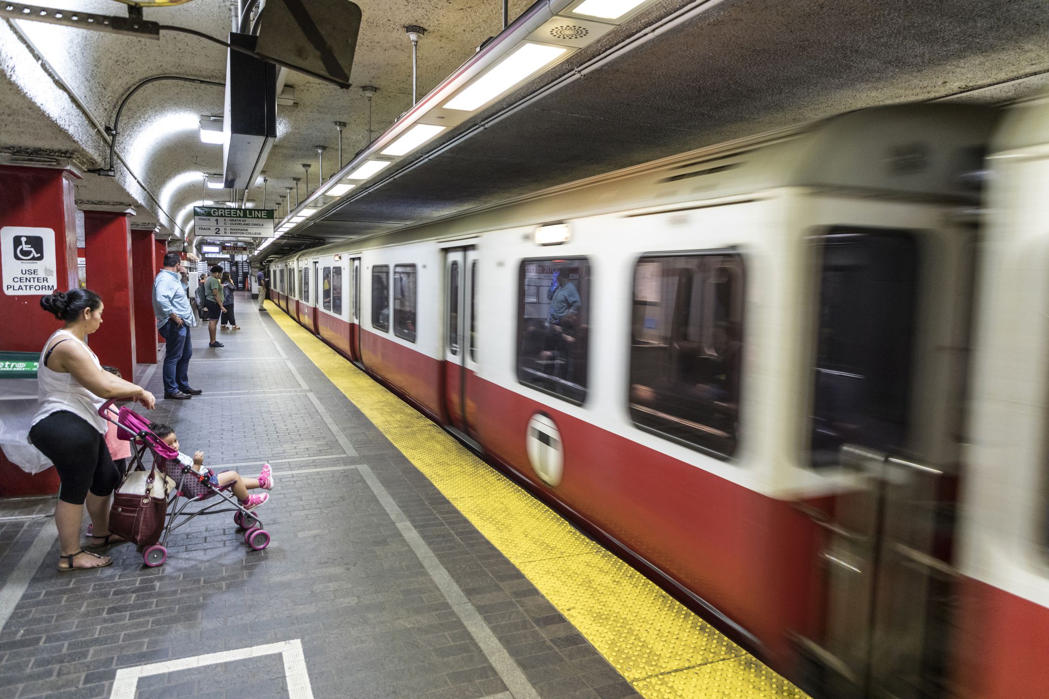 woman with stroller standing next to handicap sign prepares to board red line boston train