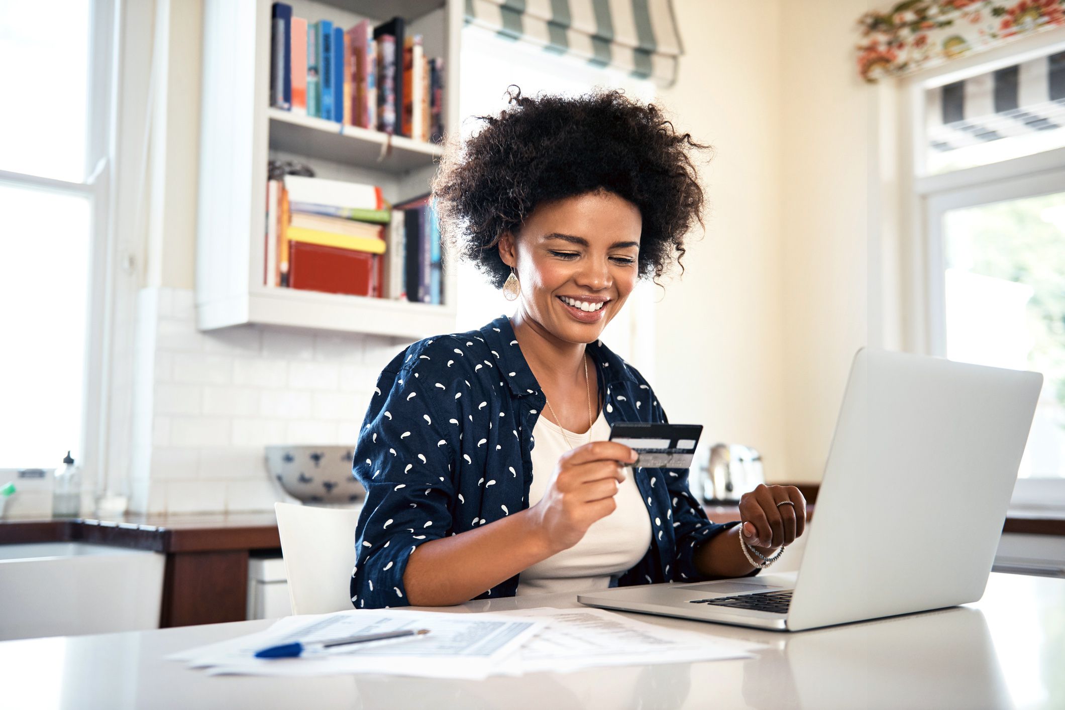 smiling woman signing up for credit card with laptop and papers on desk