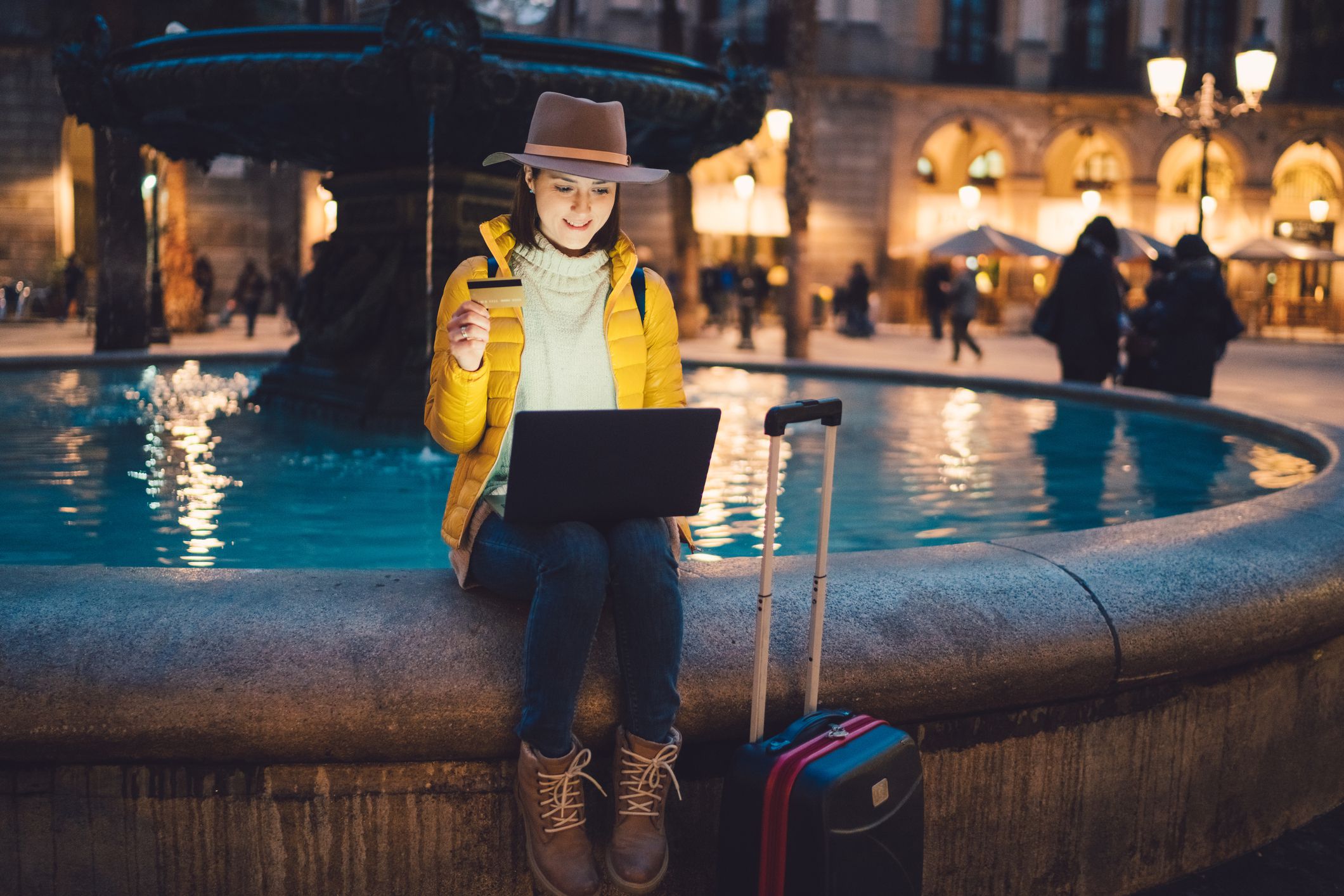 tourist sitting on fountain in barcelona with laptop and credit card