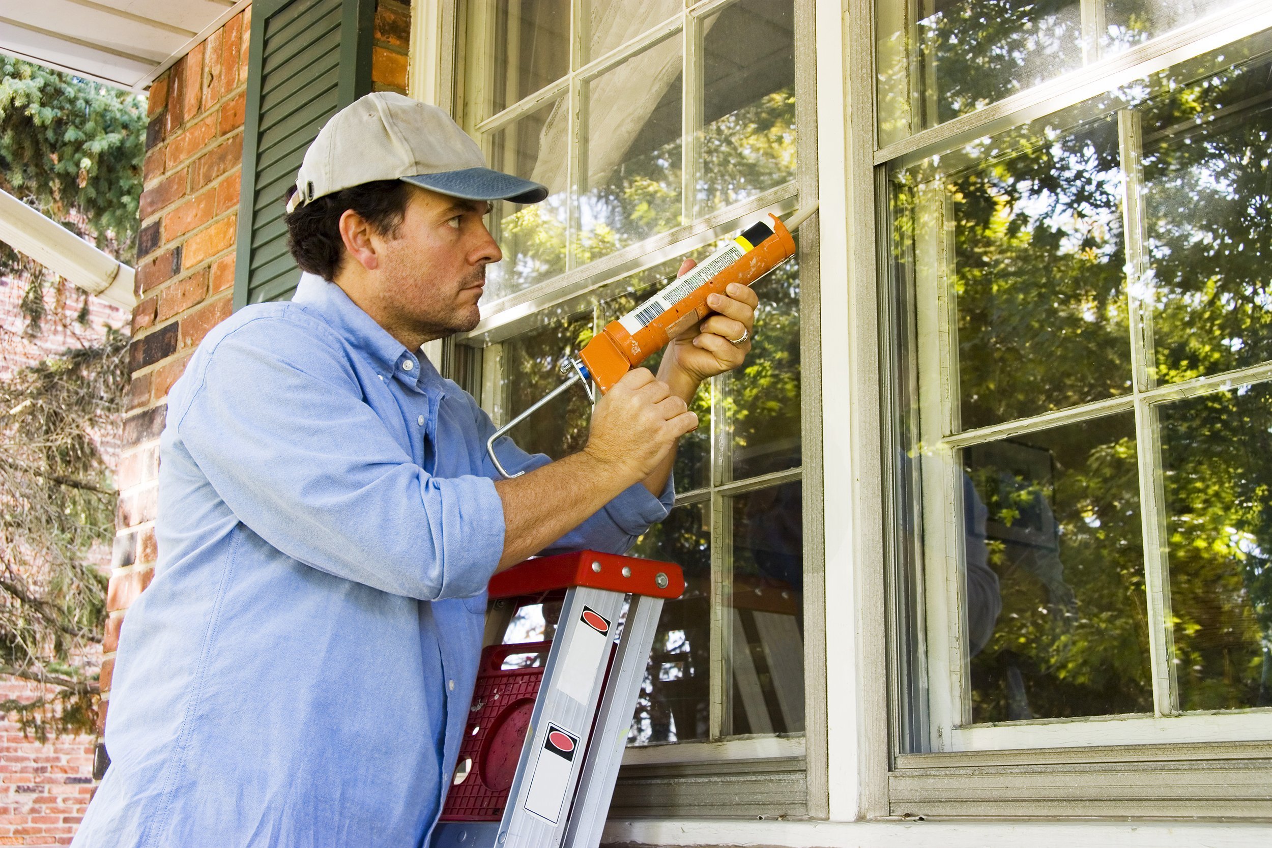 man on ladder caulking outside window