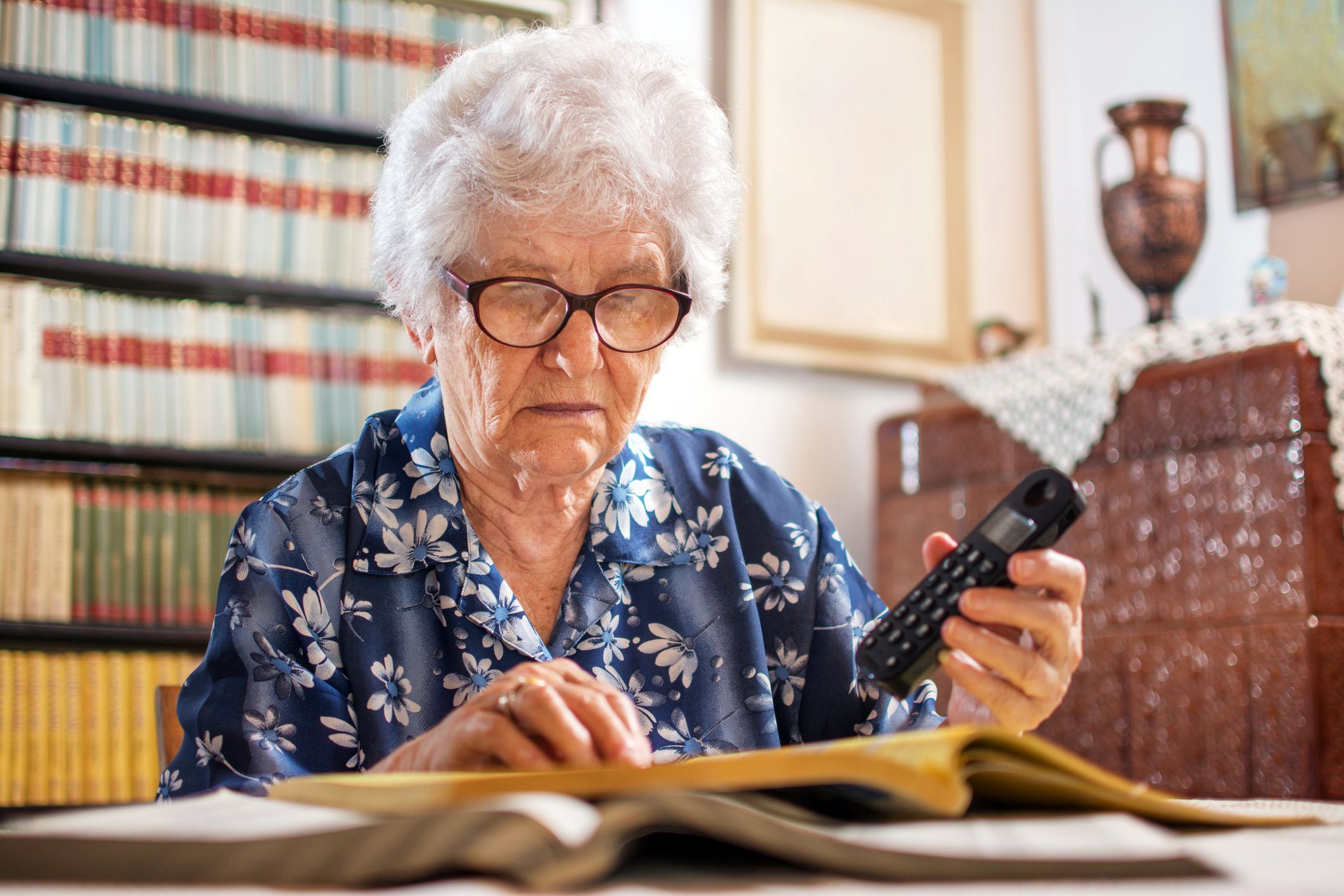 elderly woman looking through phonebook with phone in hand