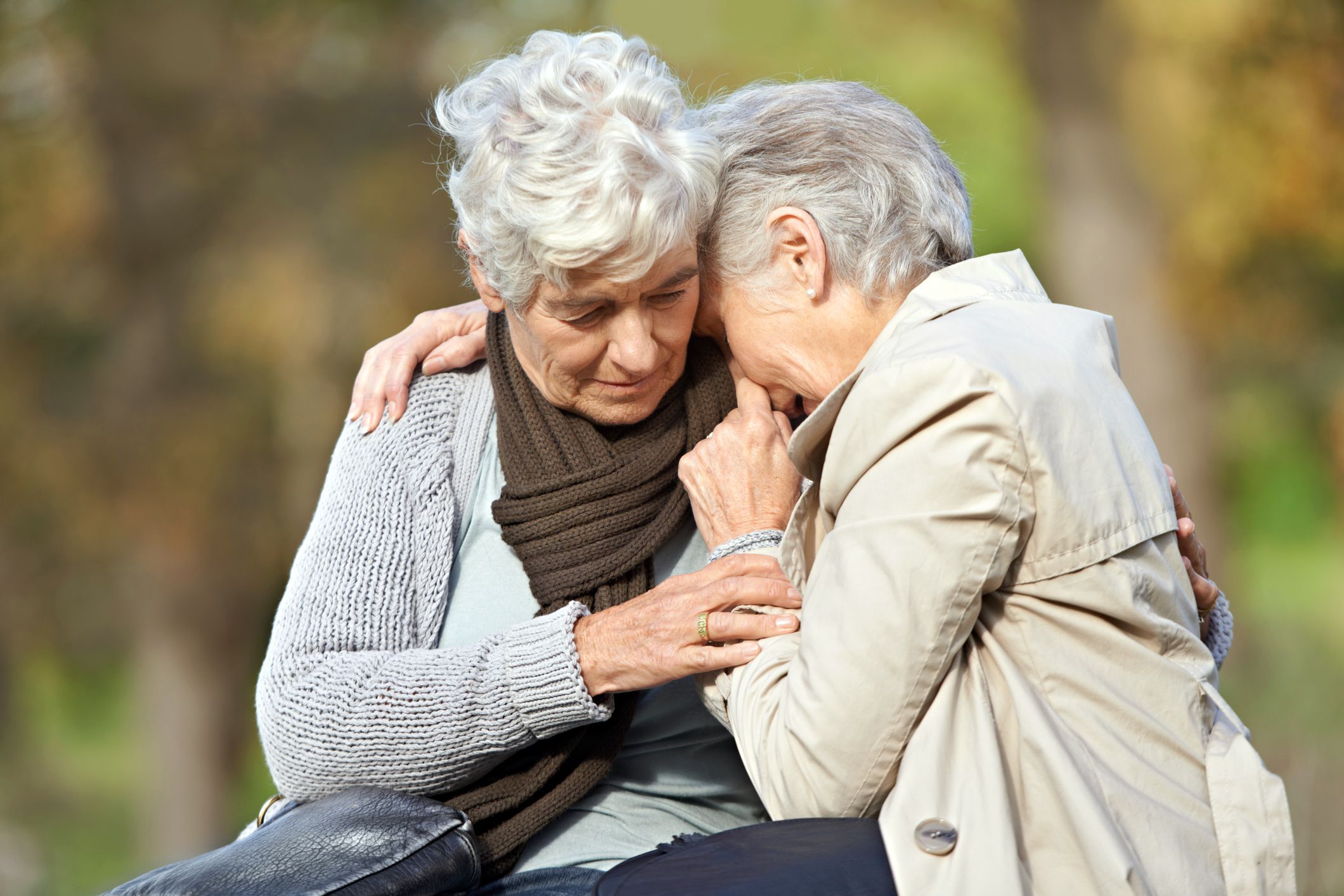one elderly woman comforting another and holding her outdoors