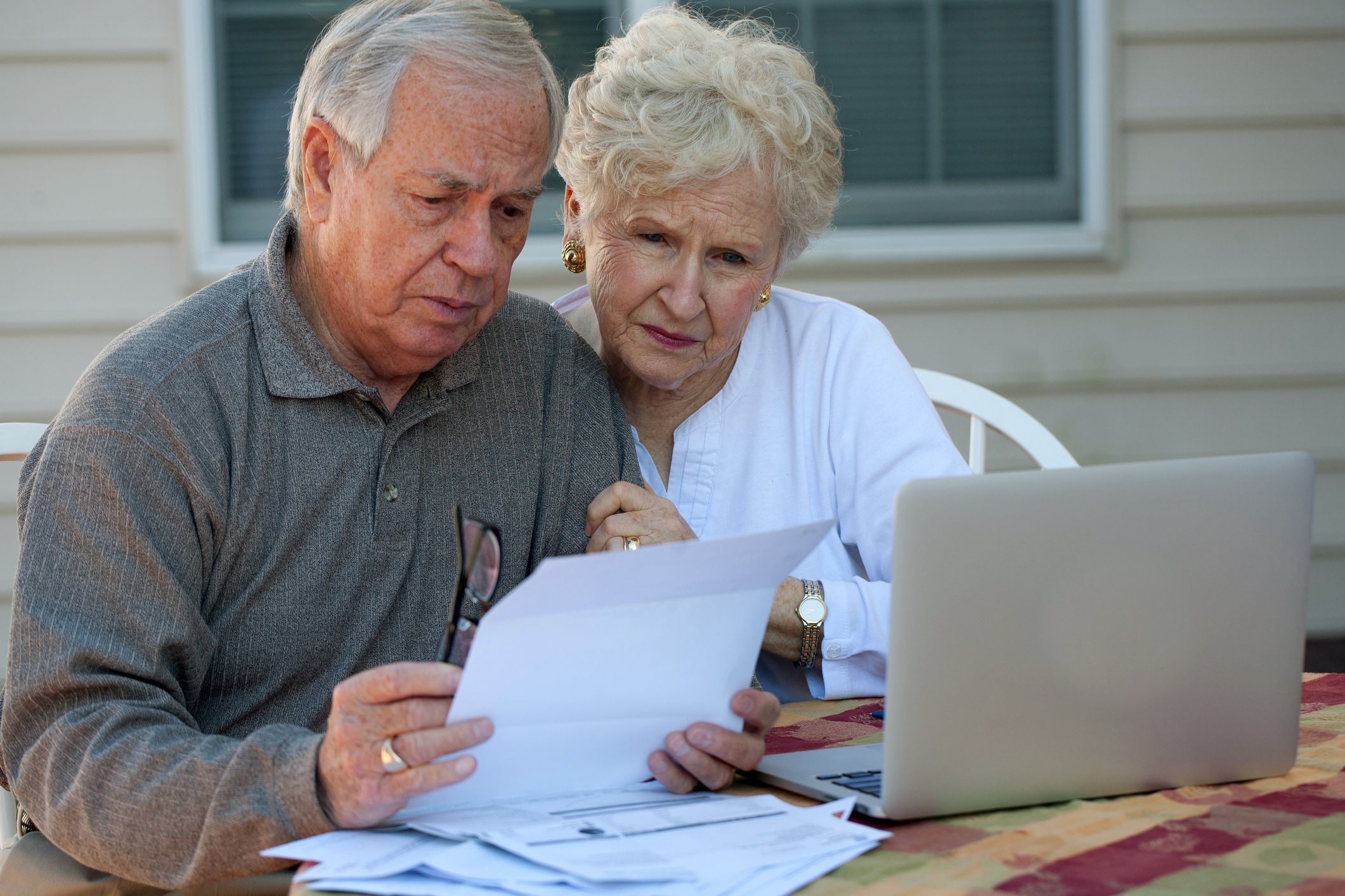 elderly couple outside looking at laptop and papers with serious expressions