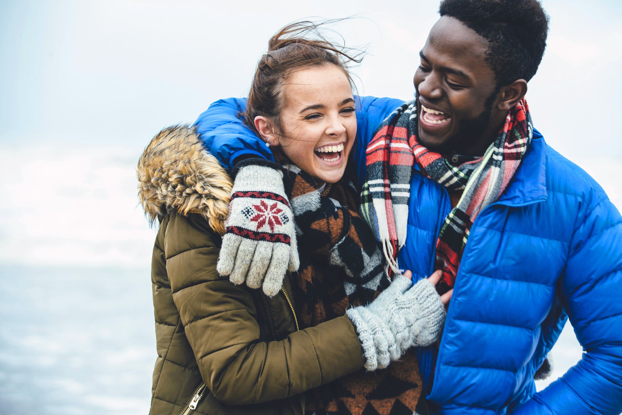 smiling couple in winter clothes at beach