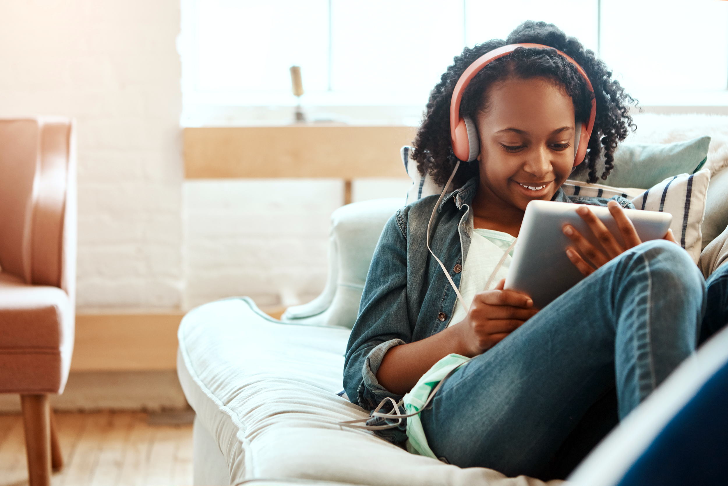 Young girl on the couch using her tablet and wearing headphones