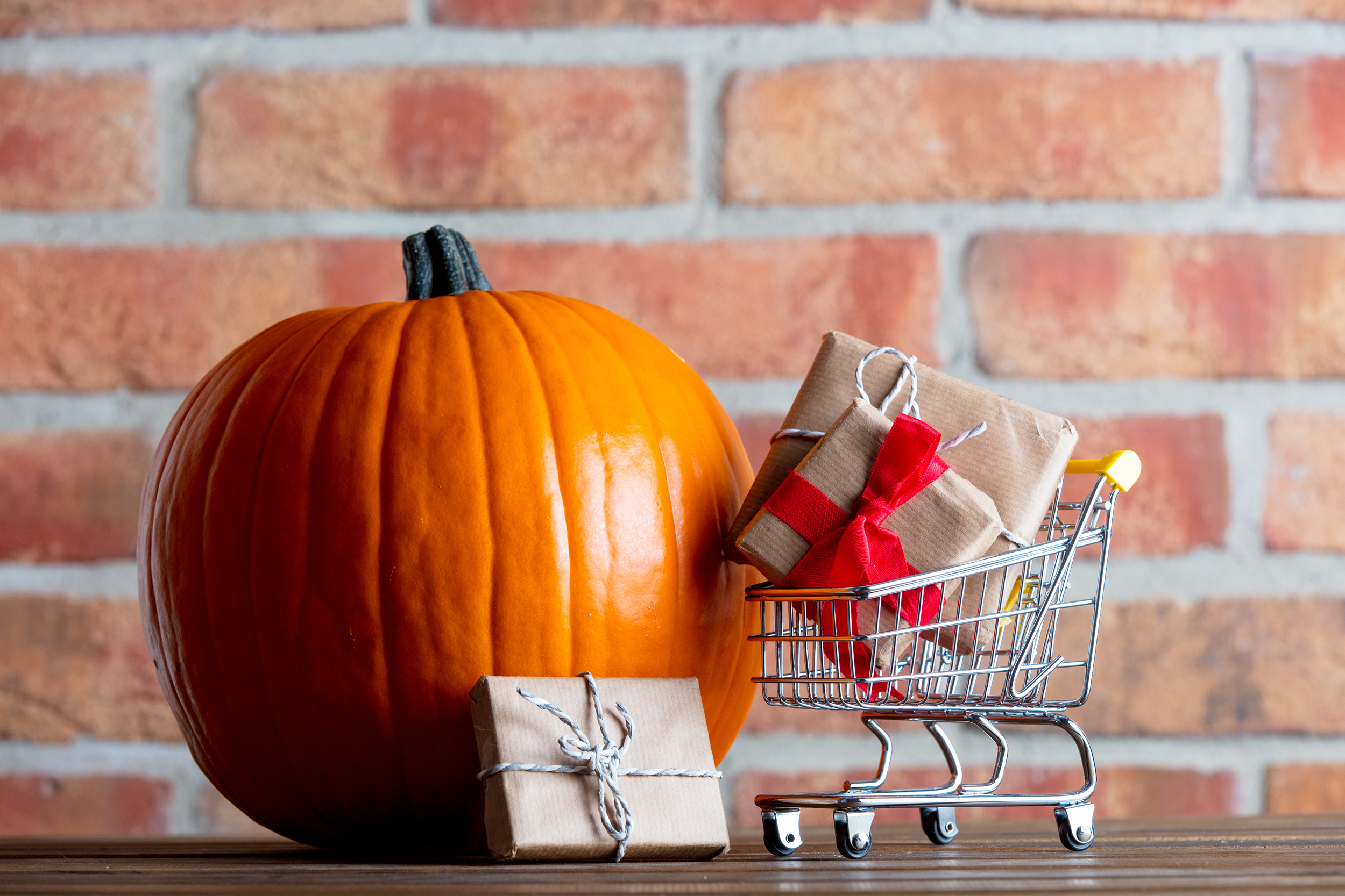 Pumpkin in front of a brick wall with a miniature shopping cart and presents
