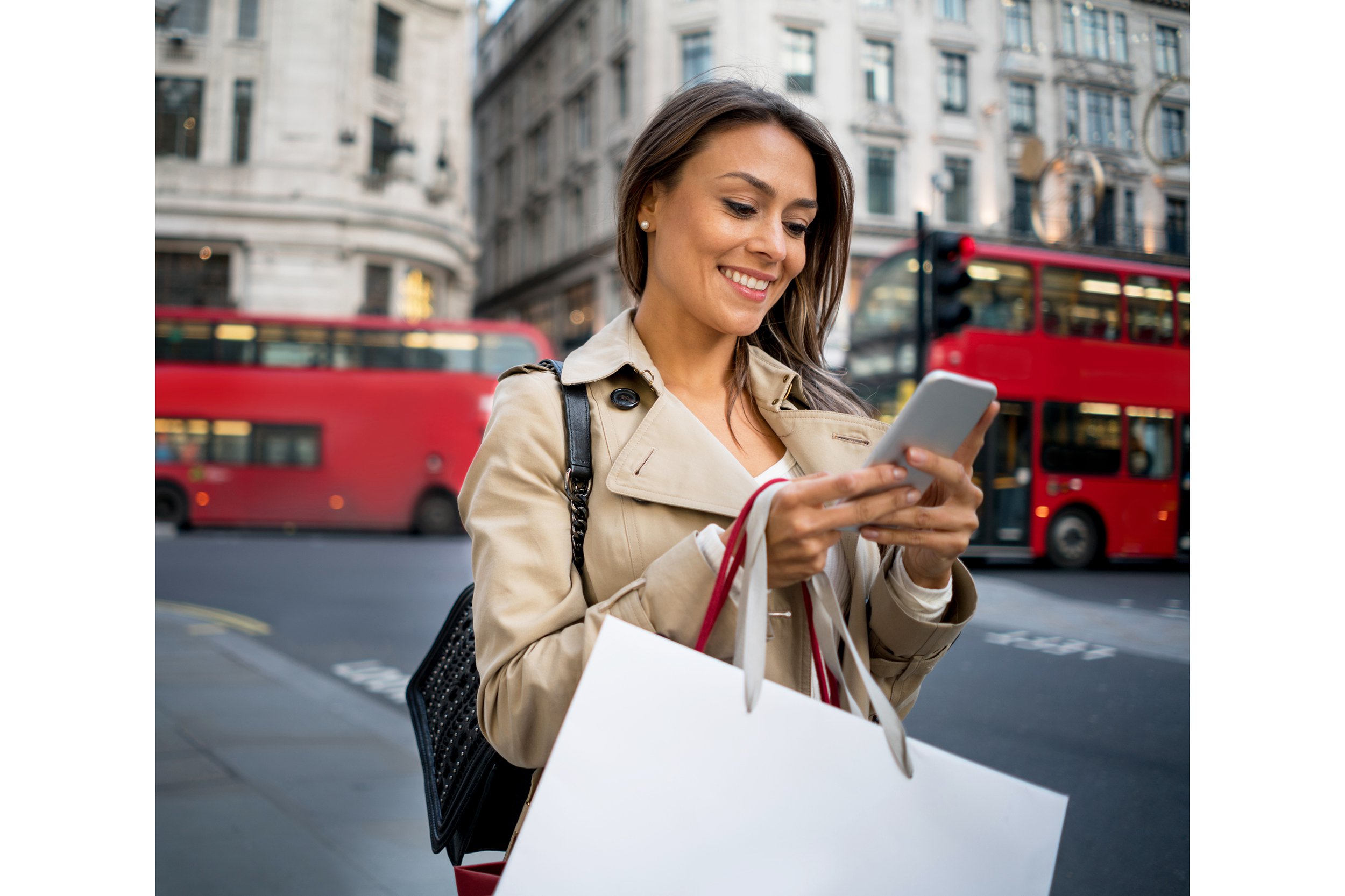Woman standing outside with shopping bags and looking at her smartphone