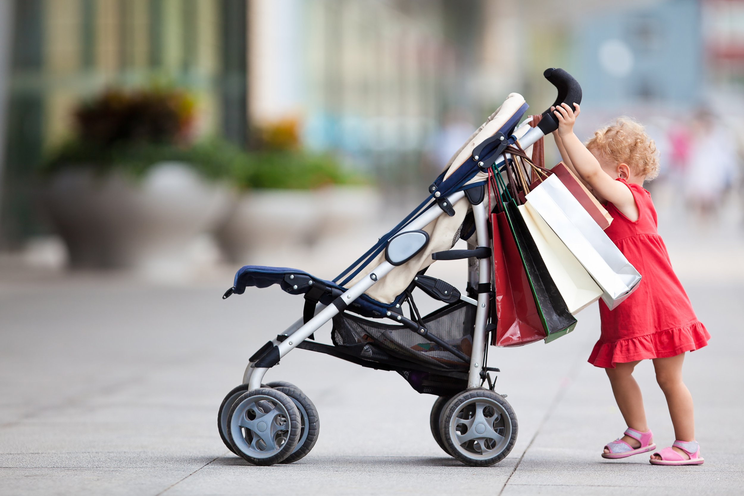 Toddler girl pushing a stroller with shopping bags attached to the handle