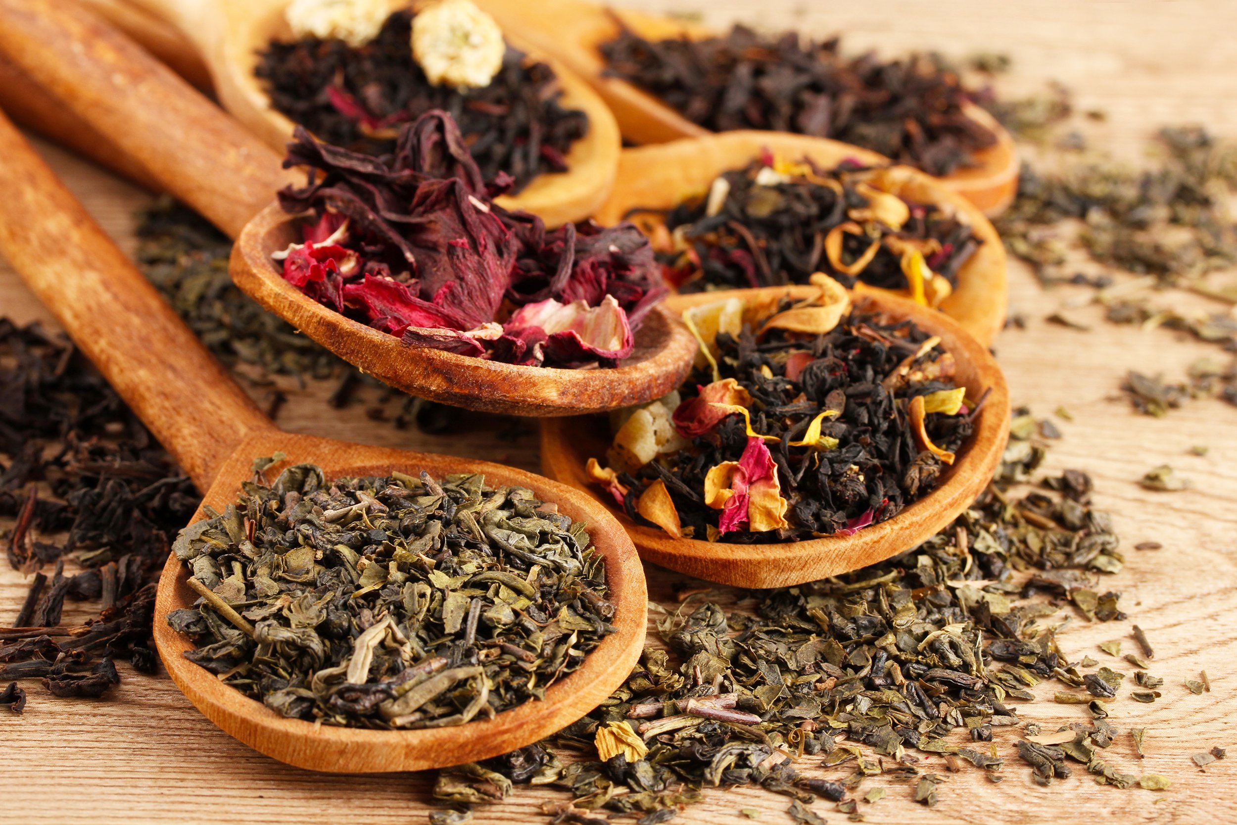 assortment of dry tea in spoons, on wooden background