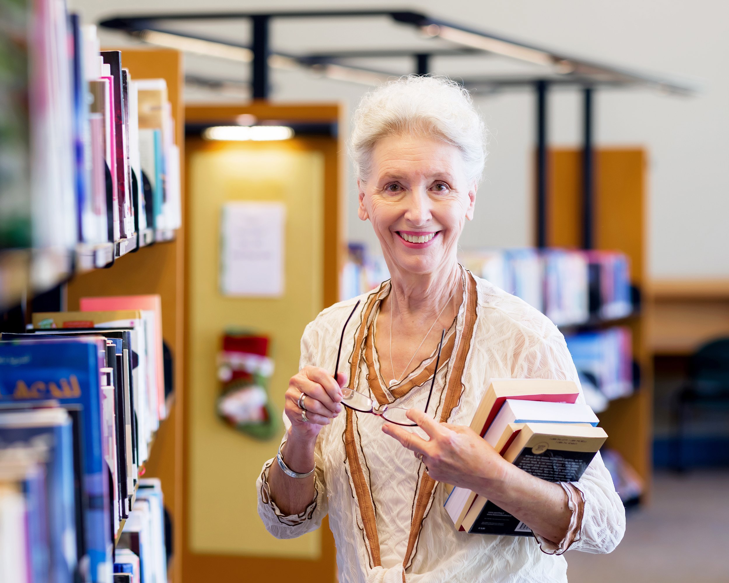 elderly lady standing next to book shelves in library