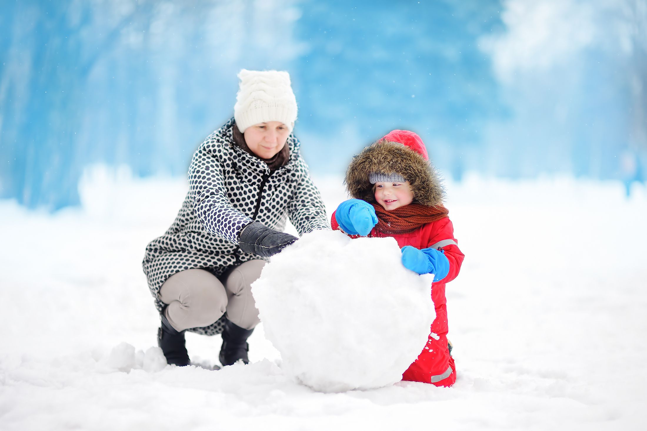 woman and toddler building snowman outside