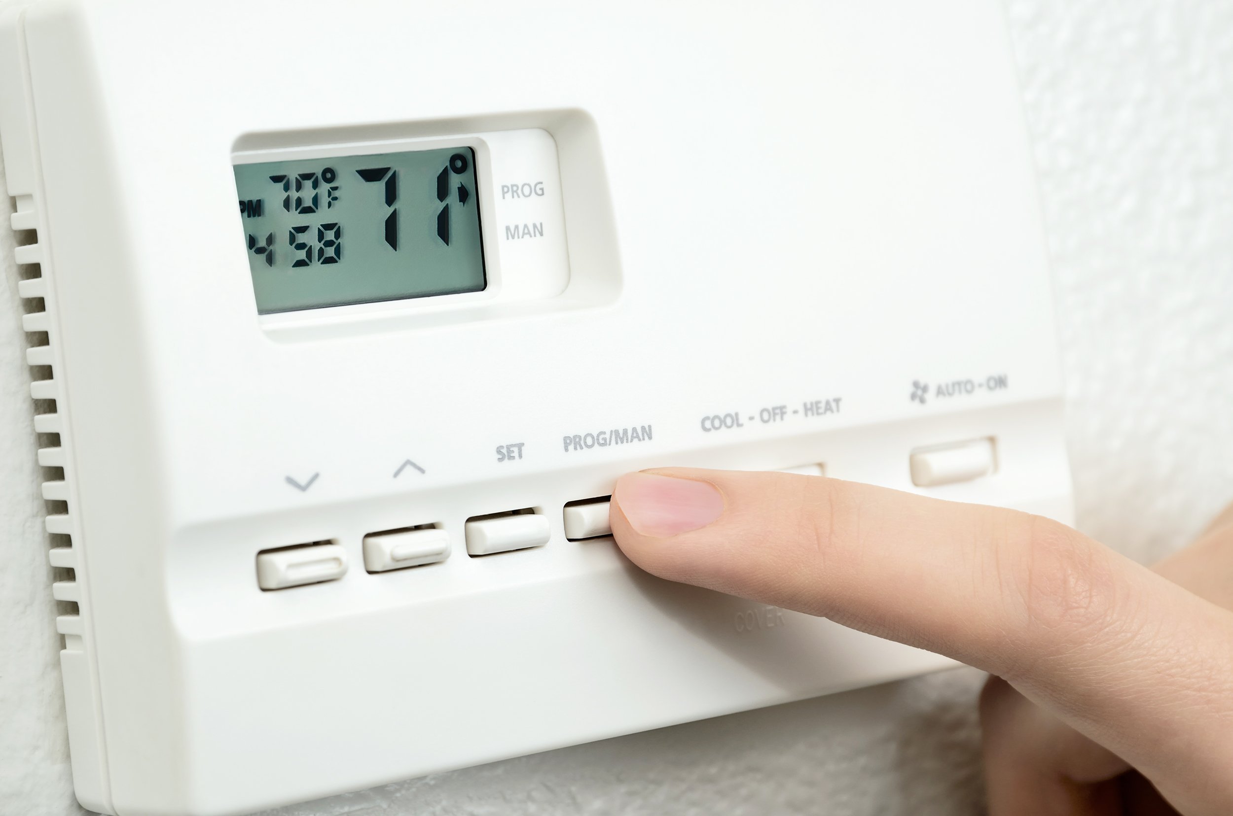 finger pressing button on digital thermostat