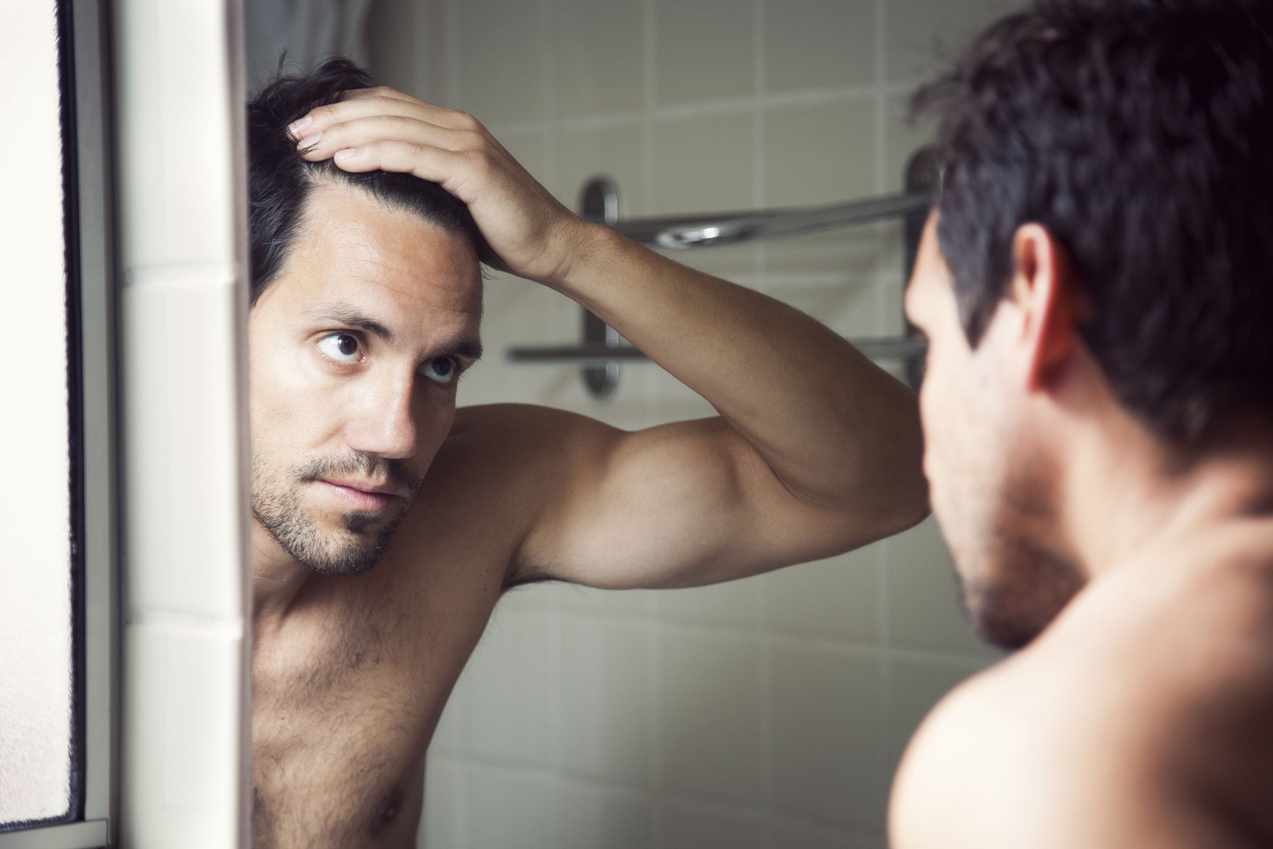 man checking hairline in bathroom mirror