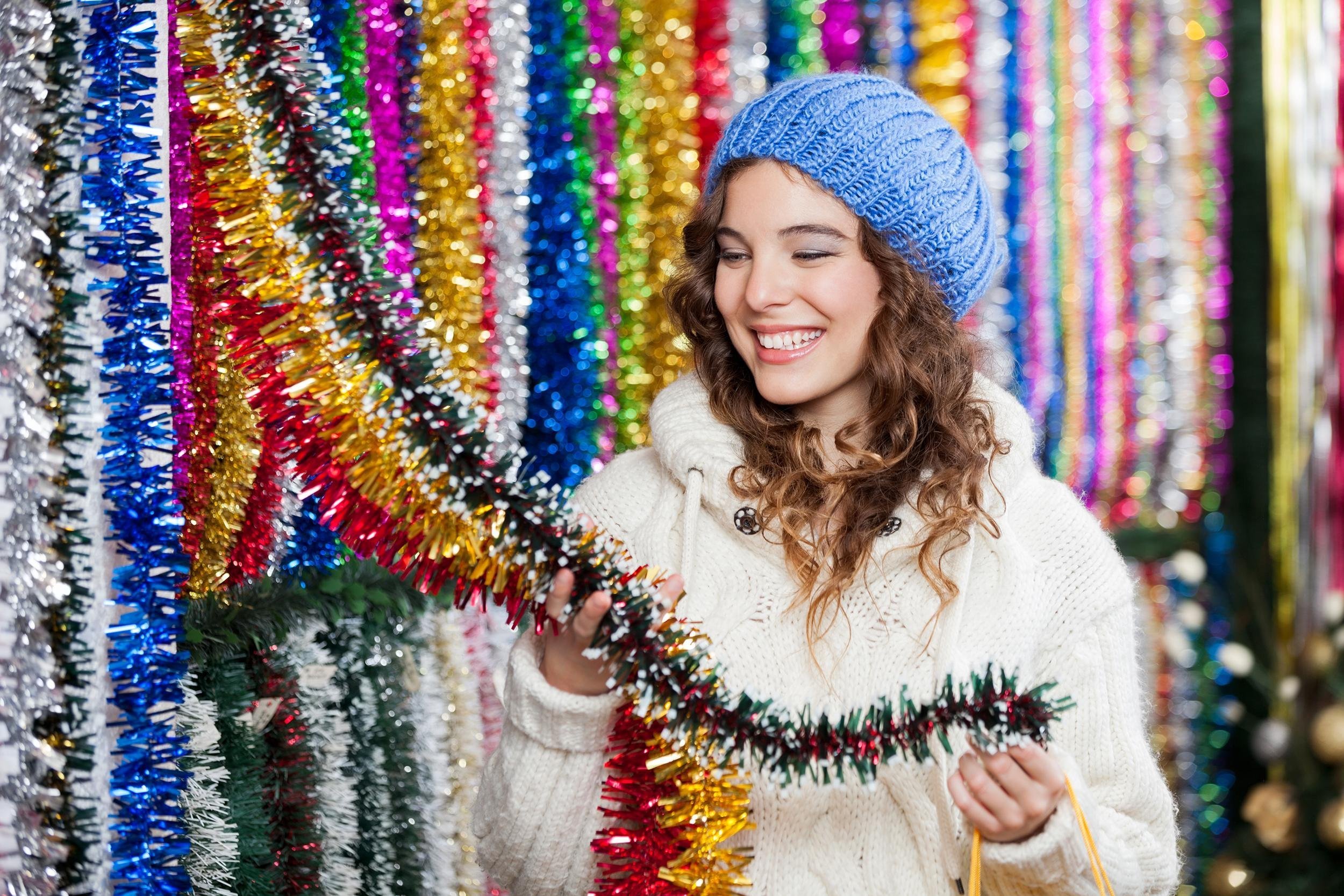 happy young woman choosing tinsels at Christmas store
