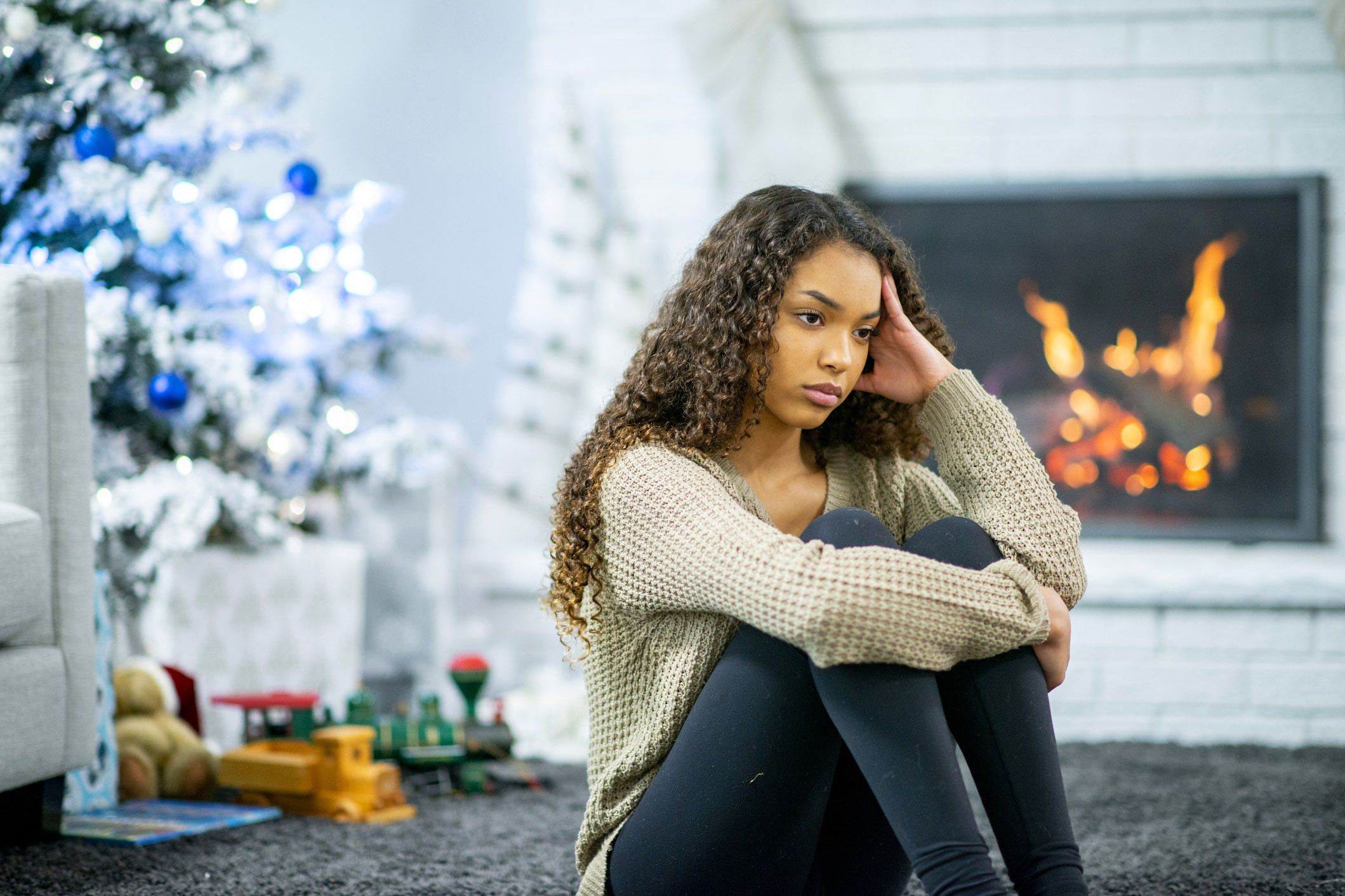 woman sitting with tense expression and hand to head with christmas tree and fireplace background