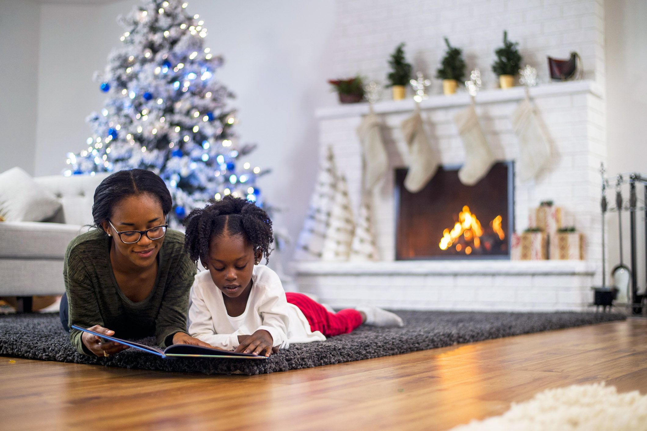 woman reading to girl on floor with christmas tree in background