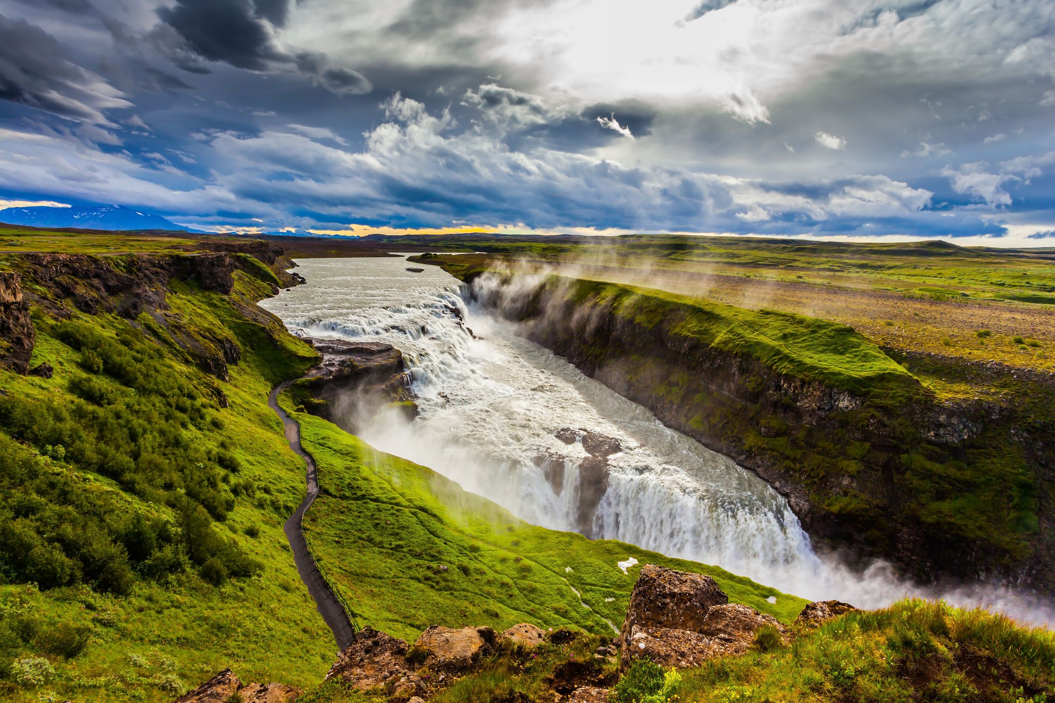 Fantastic Golden Waterfall Gulfoss in Iceland. On the shore of the waterfall is a path for tourists. Windy summer day.