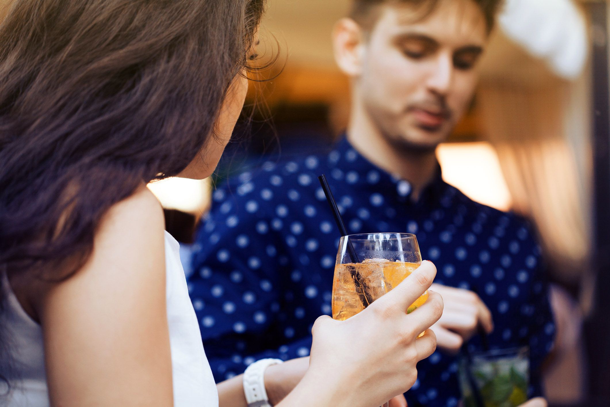 youn woman holing cocktail with man smiling in background