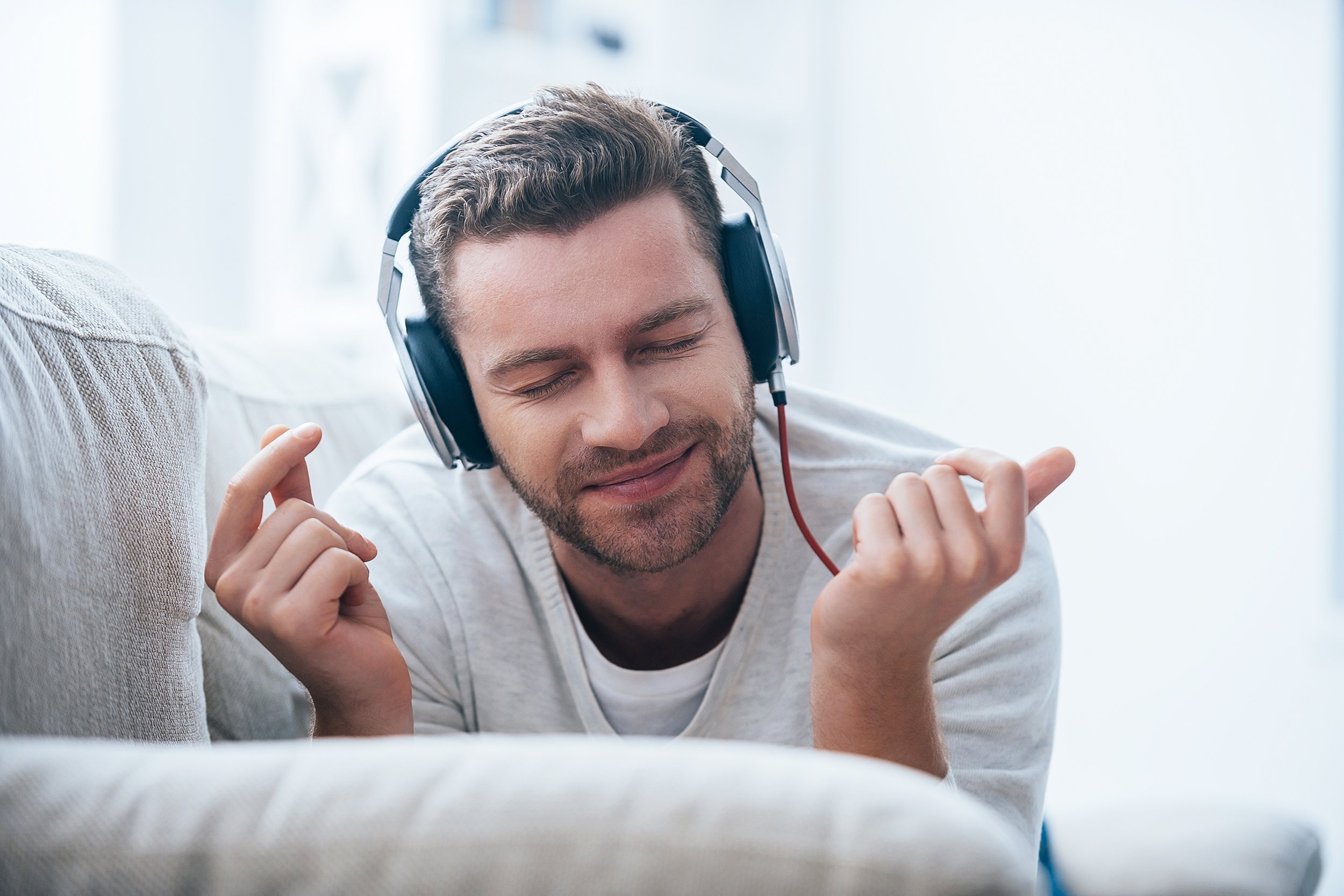 man in headphones listening to the music and gesturing while lying on his couch at home