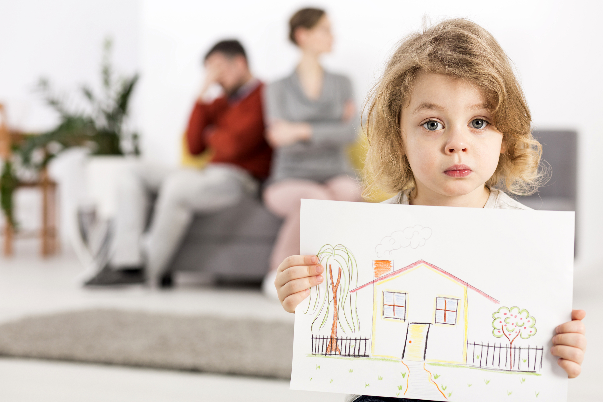 Little girl holding a picture of her house with arguing parents in the background
