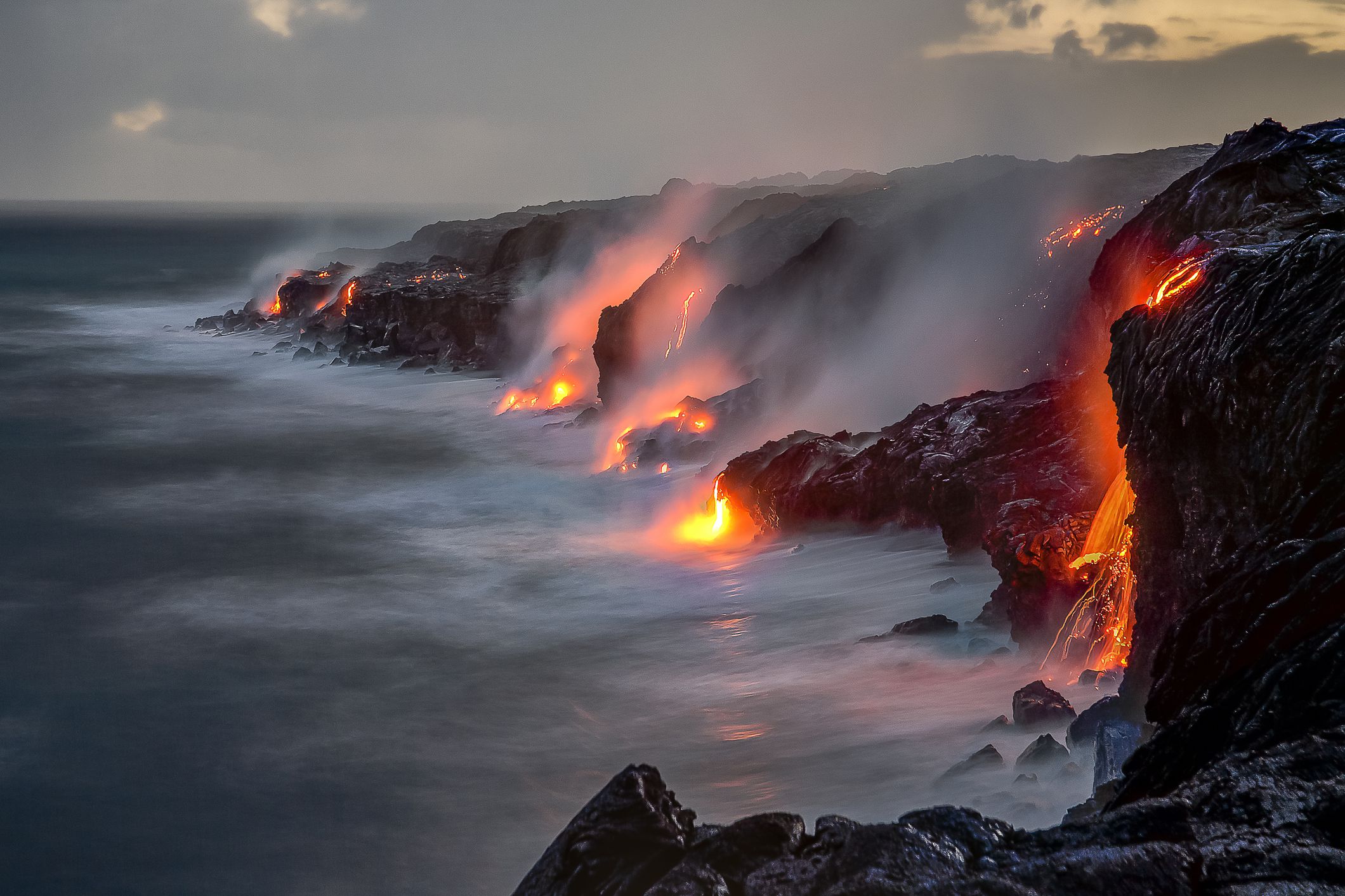 A series of lava flows spill into the ocean over a cliff at dusk, on the Big Island, Hawaii