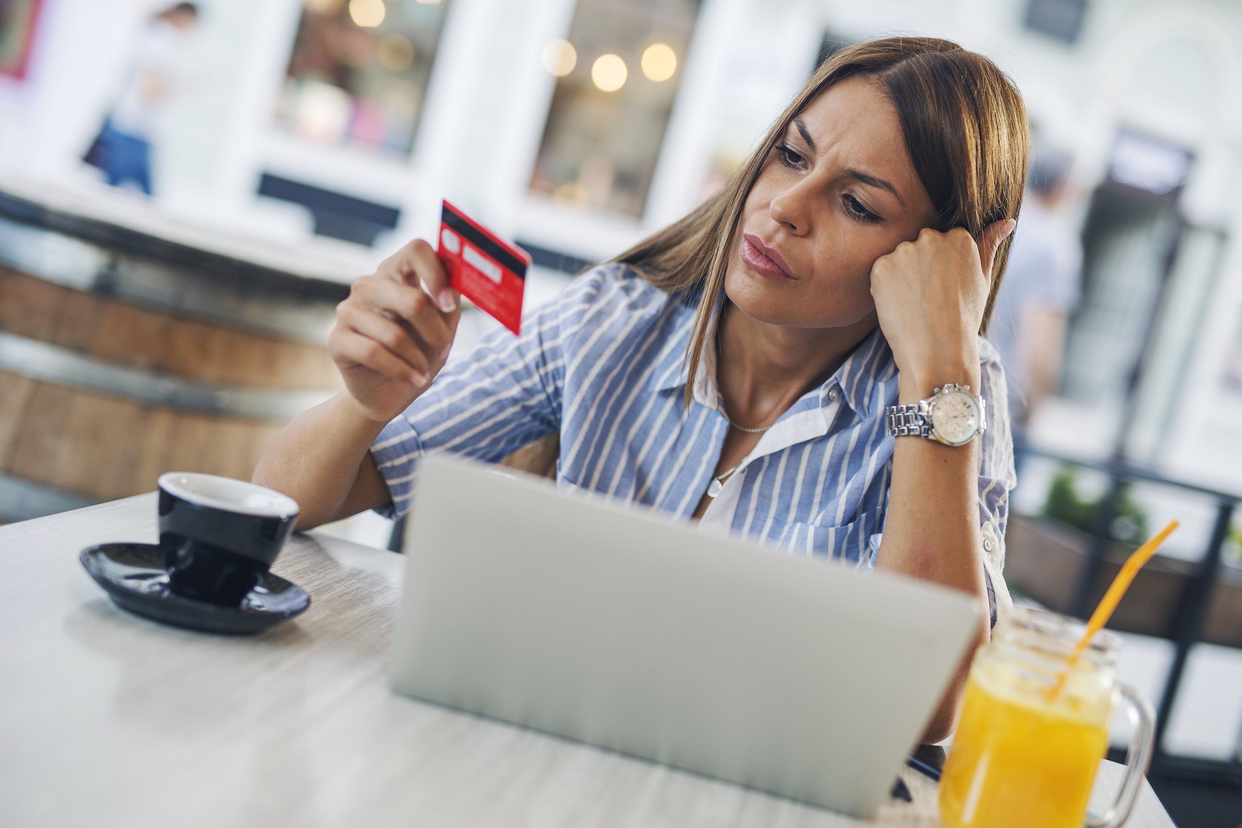 perplexed woman looking at credit card with laptop while at cafe