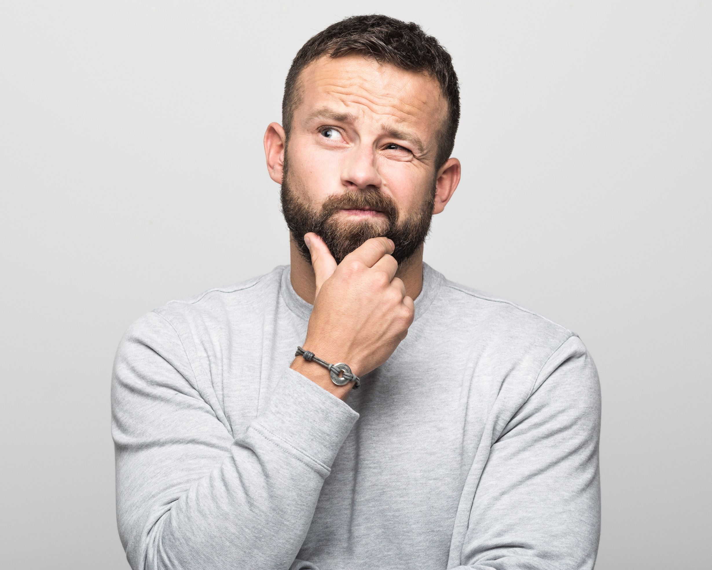 worried bearded young man looking up with hand on chin
