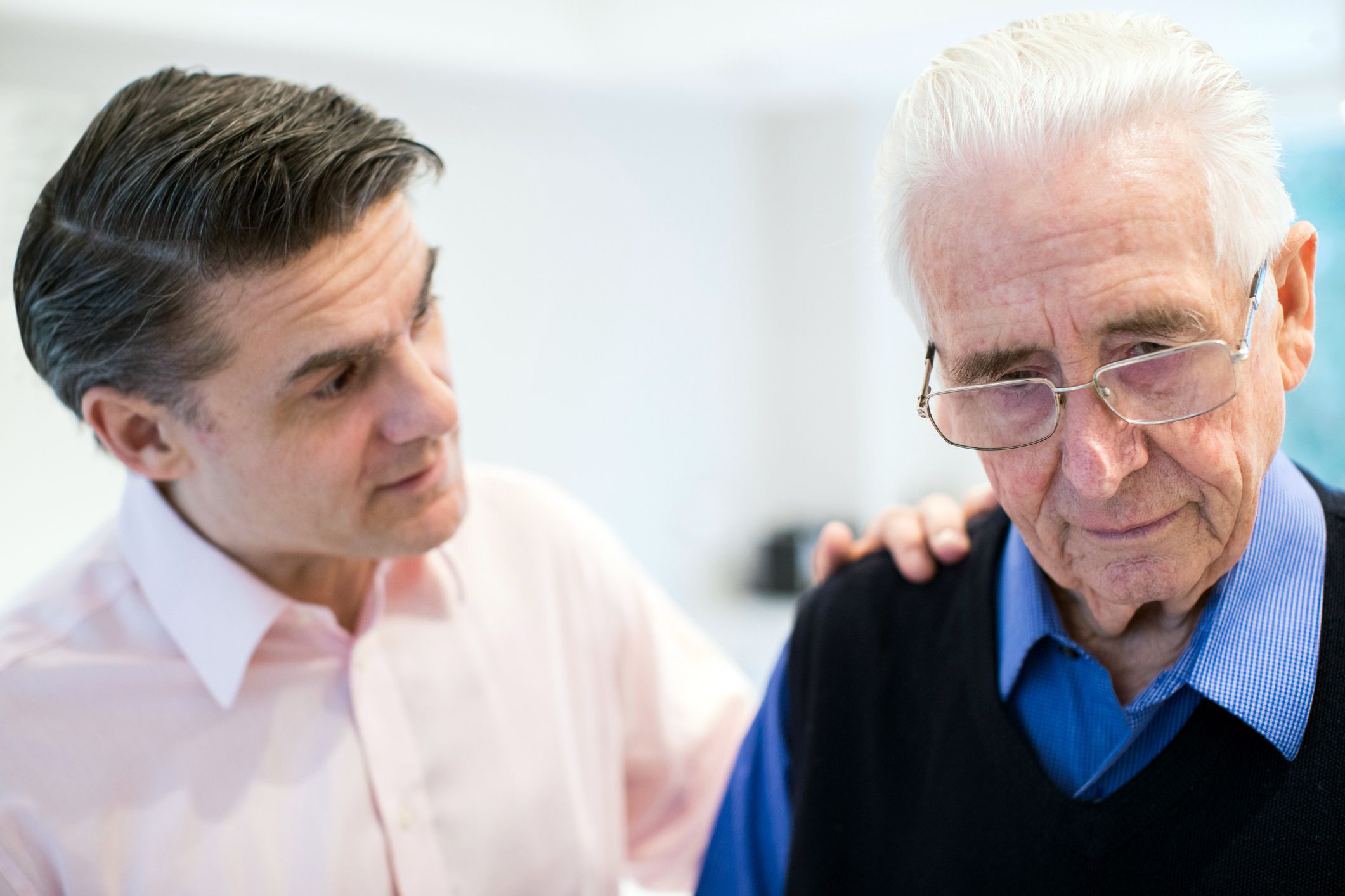Adult son with concerned face talking to senior man with serious face, blurred background of home interior