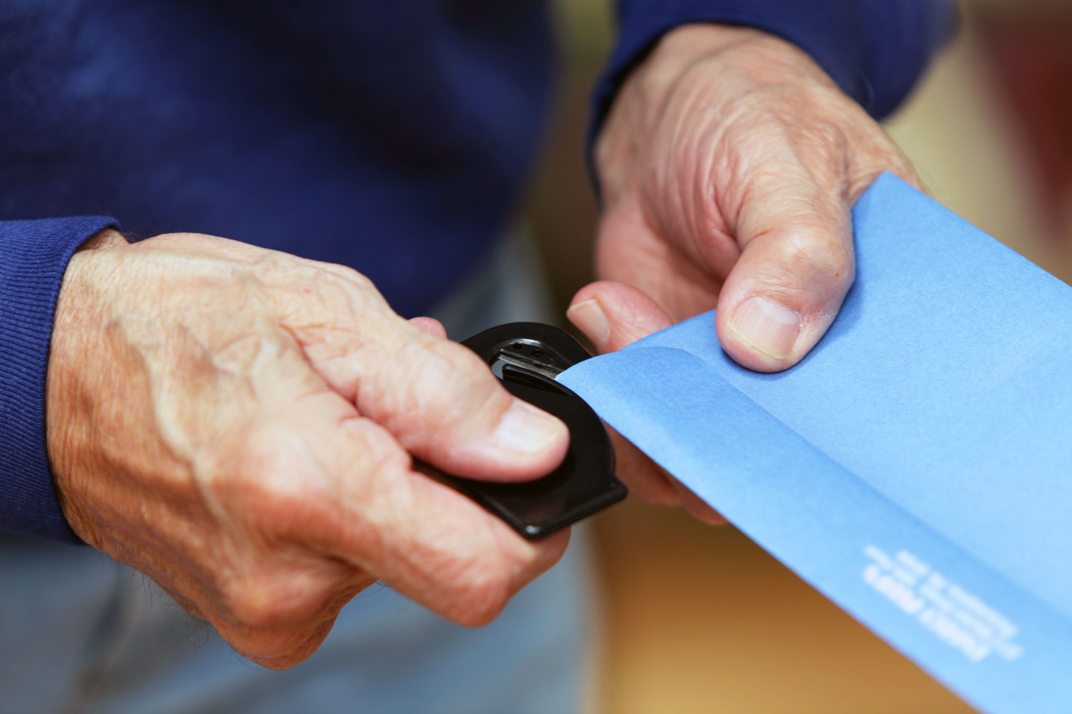 Closeup of two male senior hands opening up blue envelope