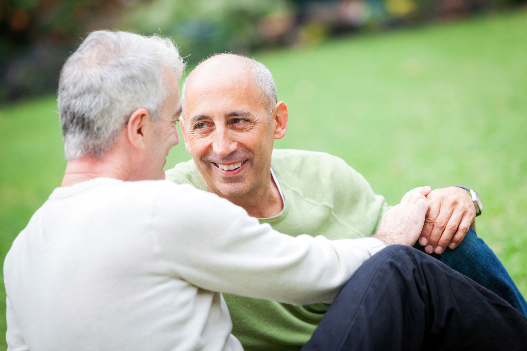 Couple in park holding hands looking at each other longingly, man with smile on his face, blurred grass in background