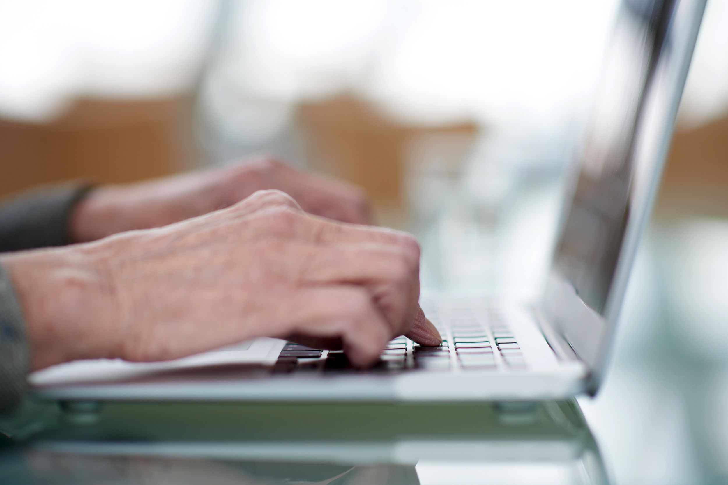 Closeup of senior hands typing on a laptop