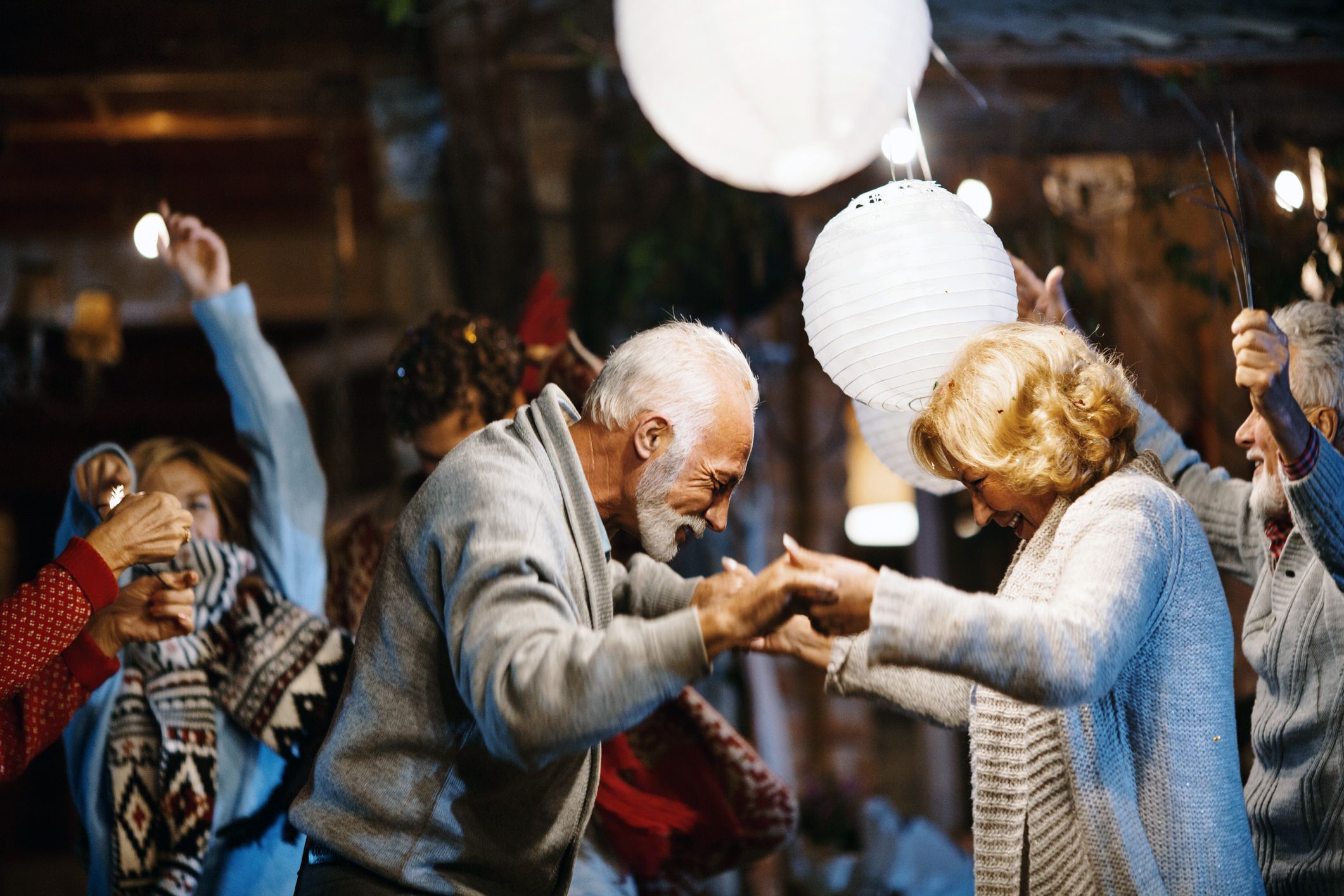 Numerous seniors dancing at a party with focus on one couple in the middle, big white paper lantern lights and blurred background