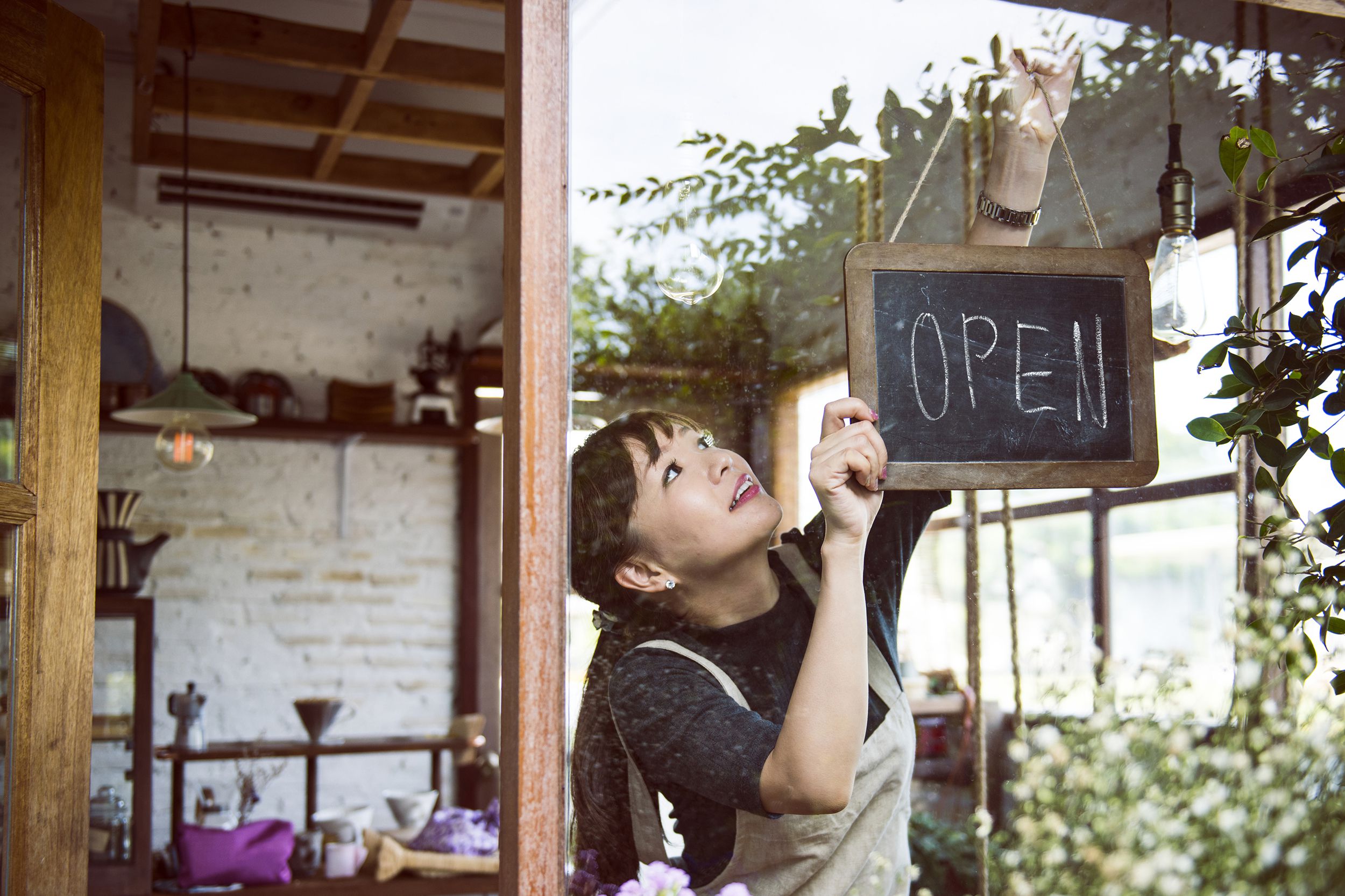 woman hanging an open sign at shop