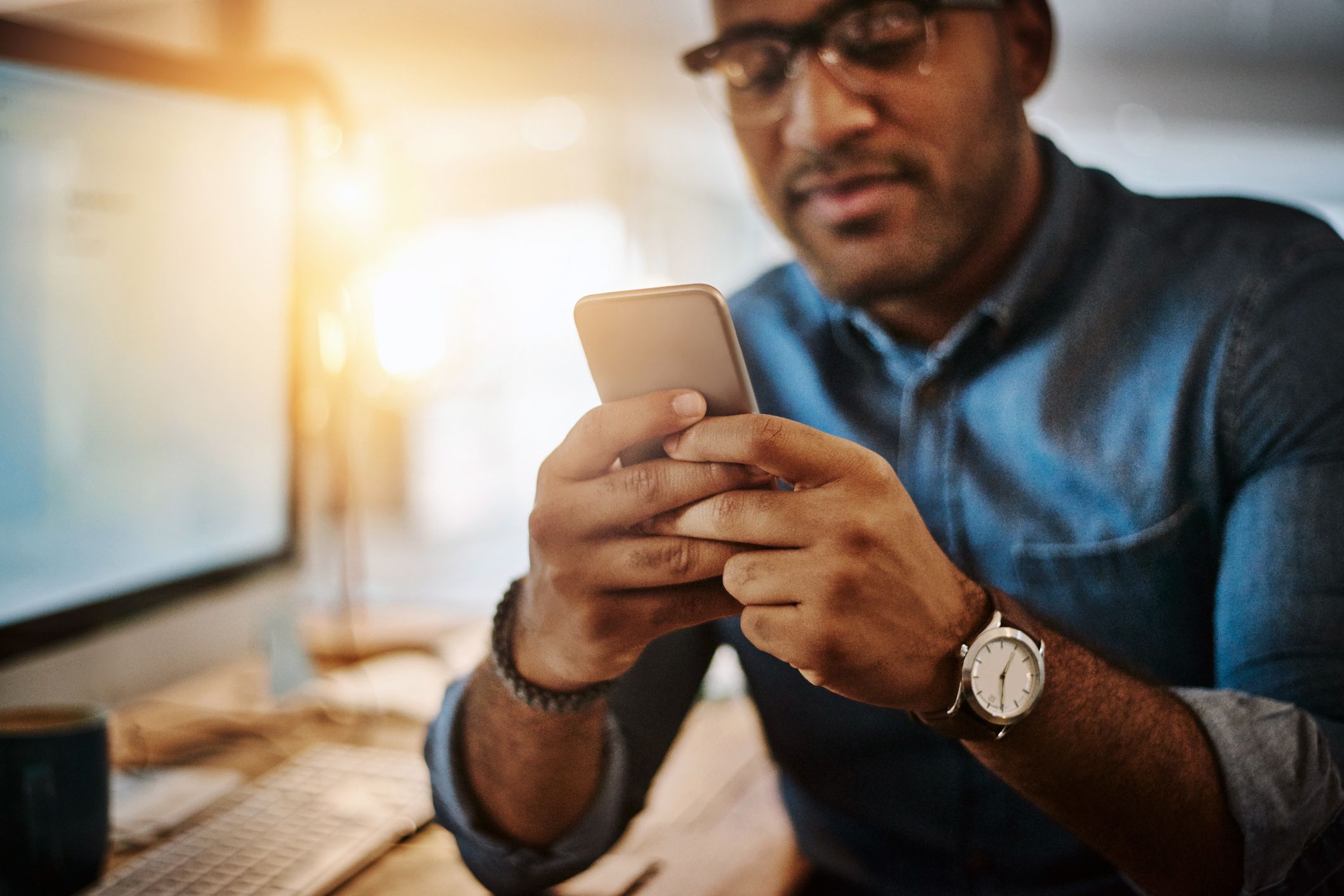 young man using app on phone, sitting at desk