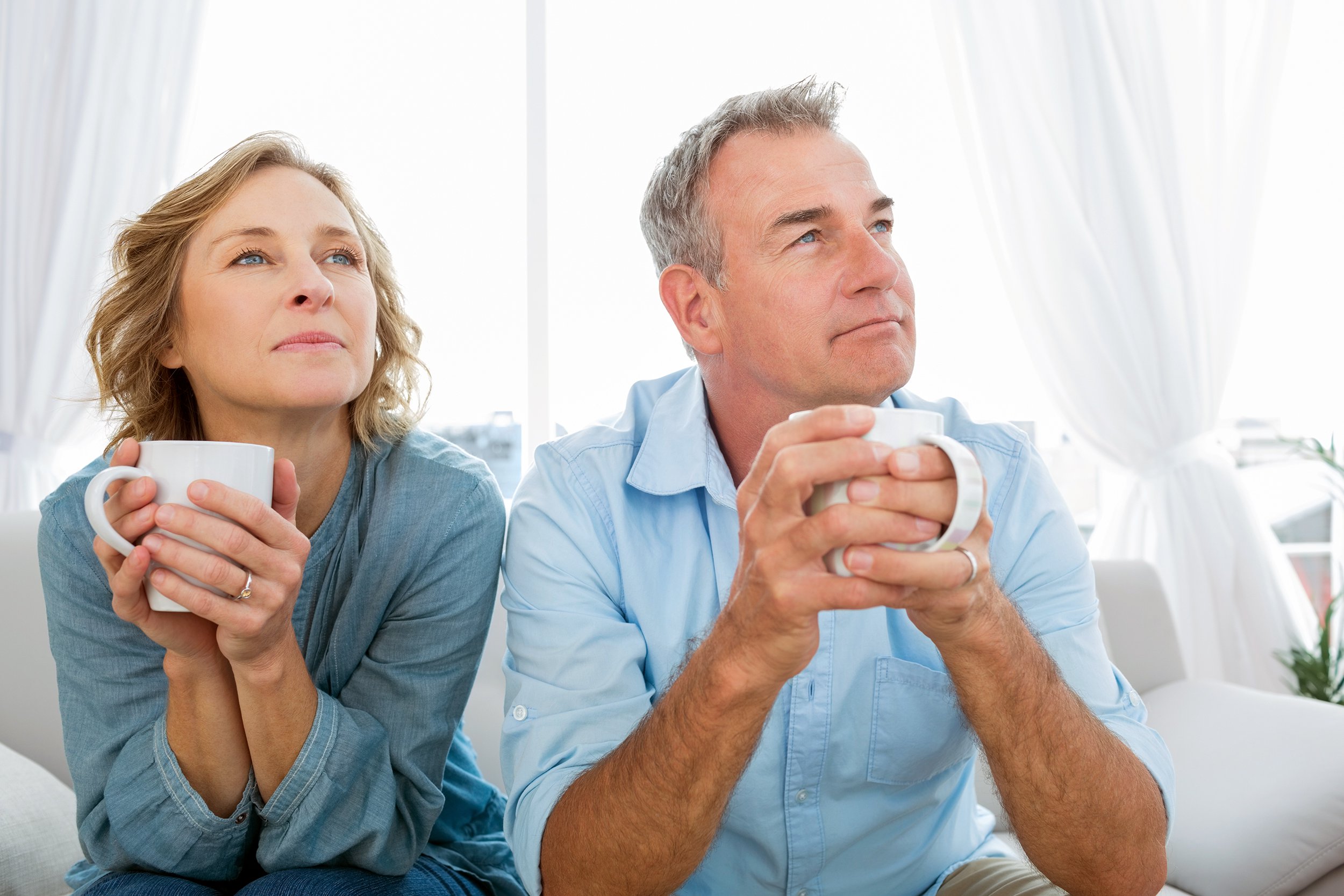 thoughtful middle-aged couple sitting on the couch having coffee