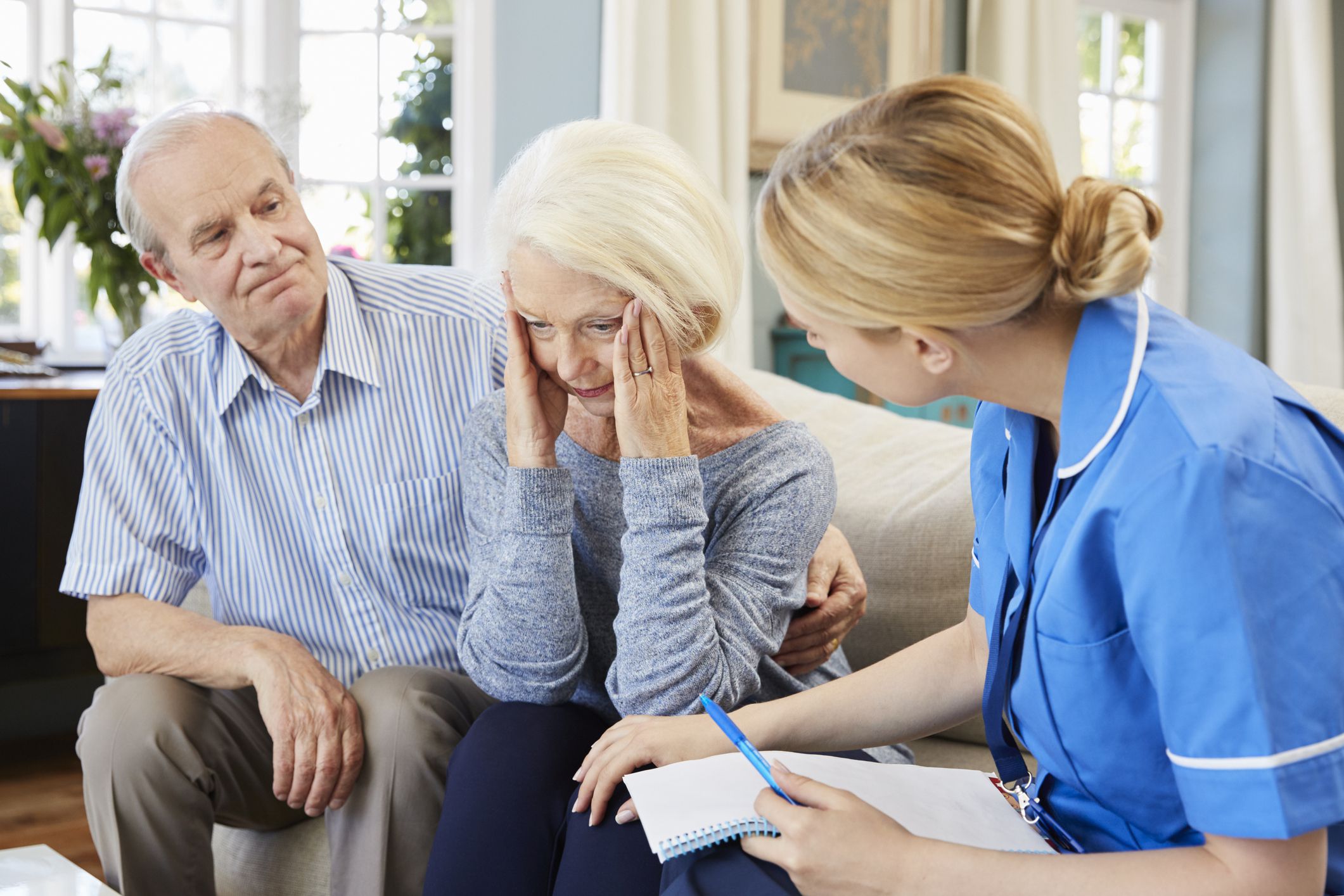 nurse speaking to senior woman with vexed expression while senior husband puts arm around her