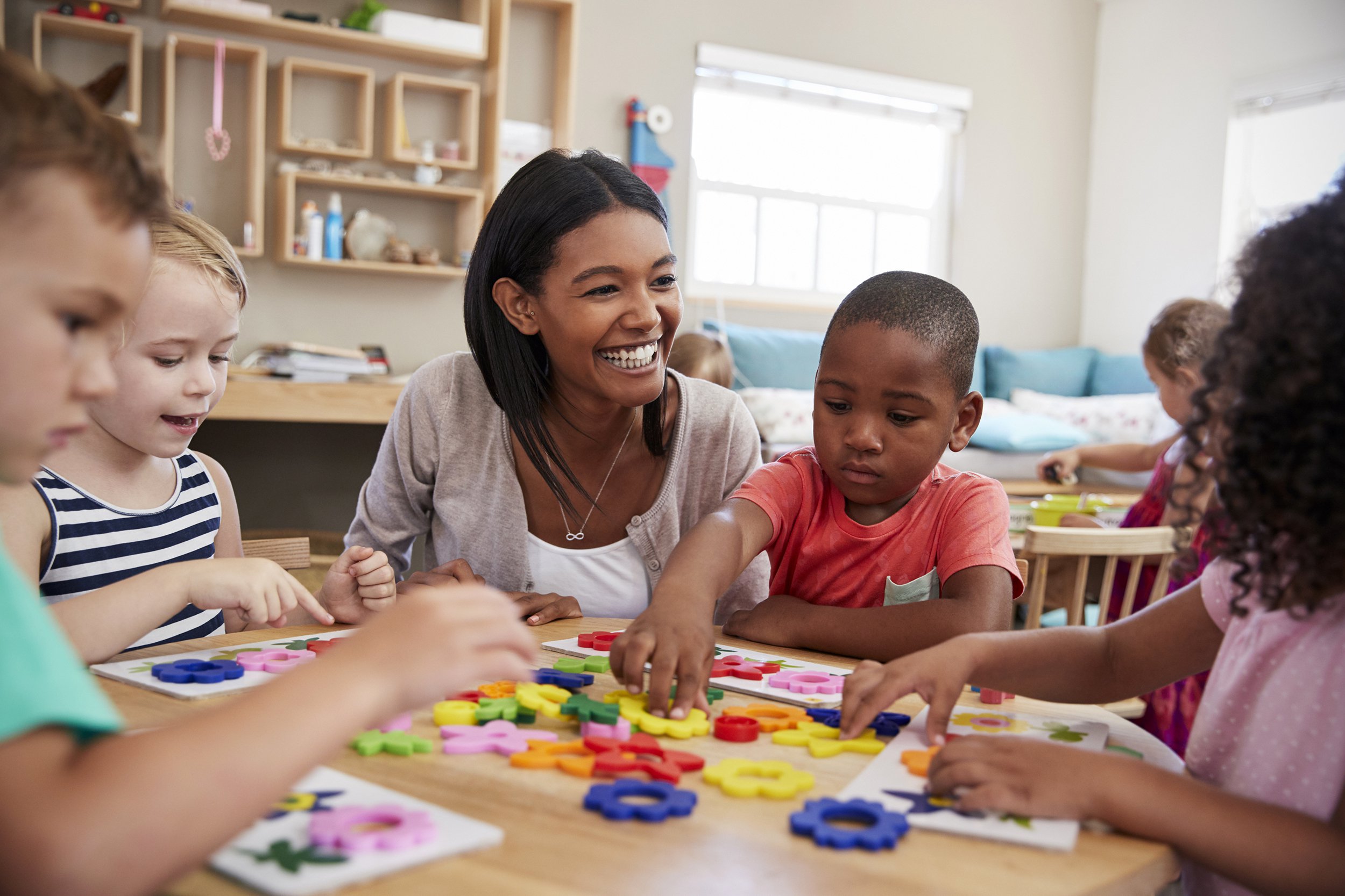Happy day care teacher sitting at a table with children