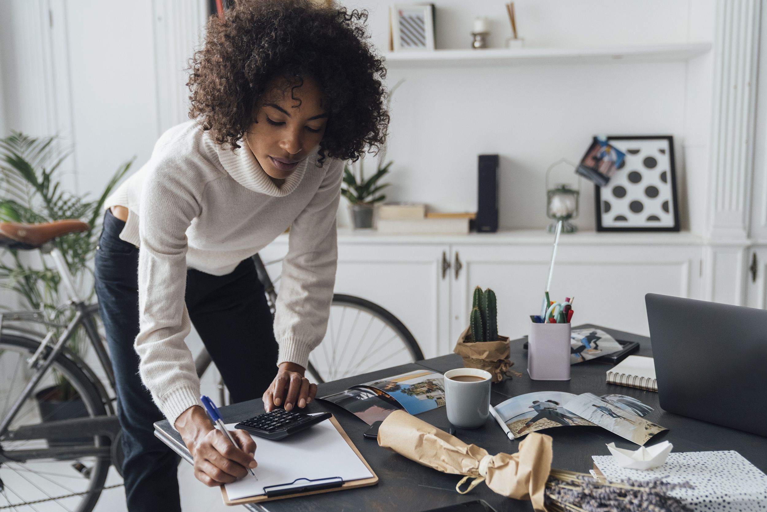 freelancer standing at her desk, using calculator, taking notes